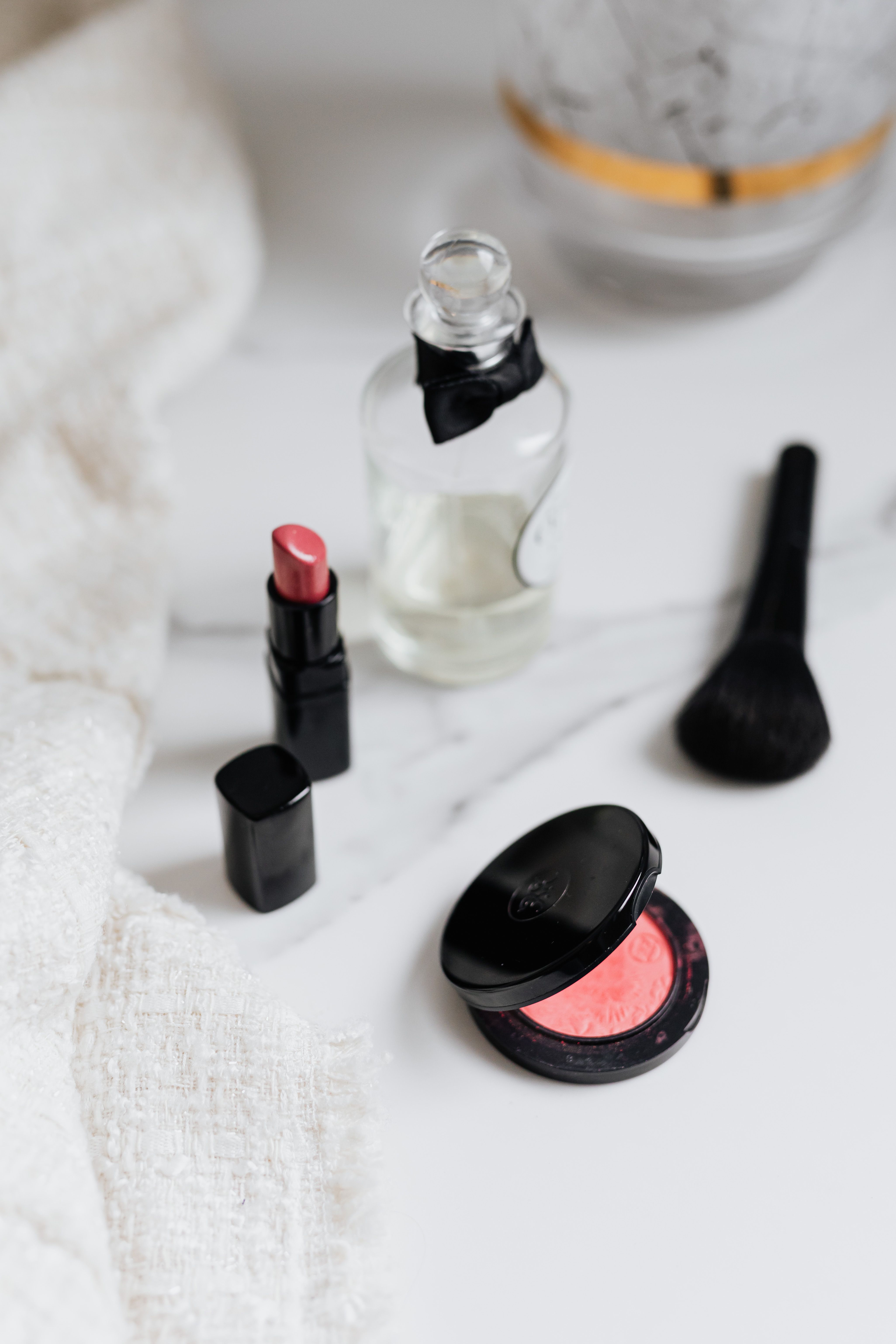 Lipstick, perfume, makeup brush and blush on a marble surface