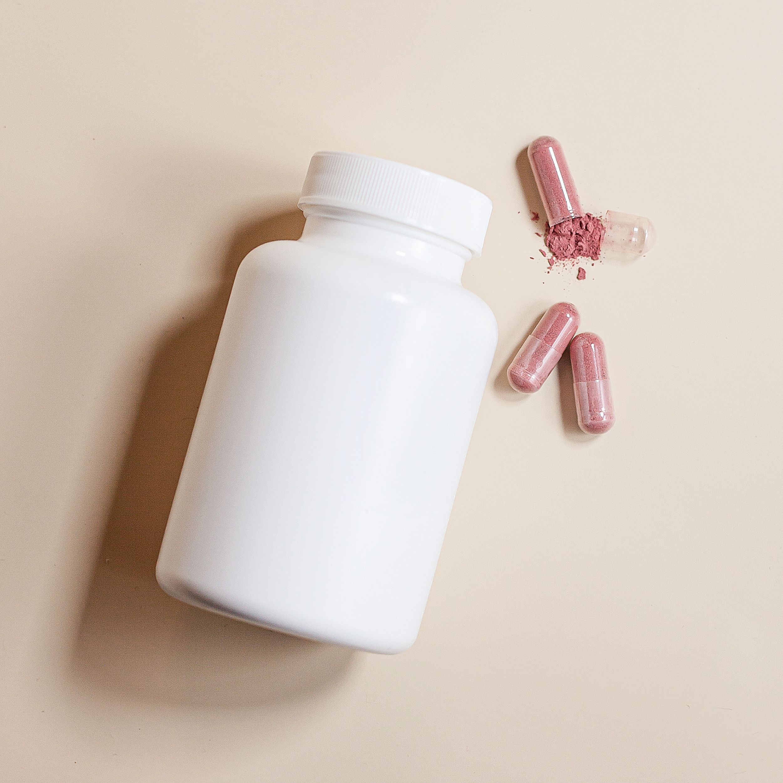 White supplement bottle with pink capsules on a peach background