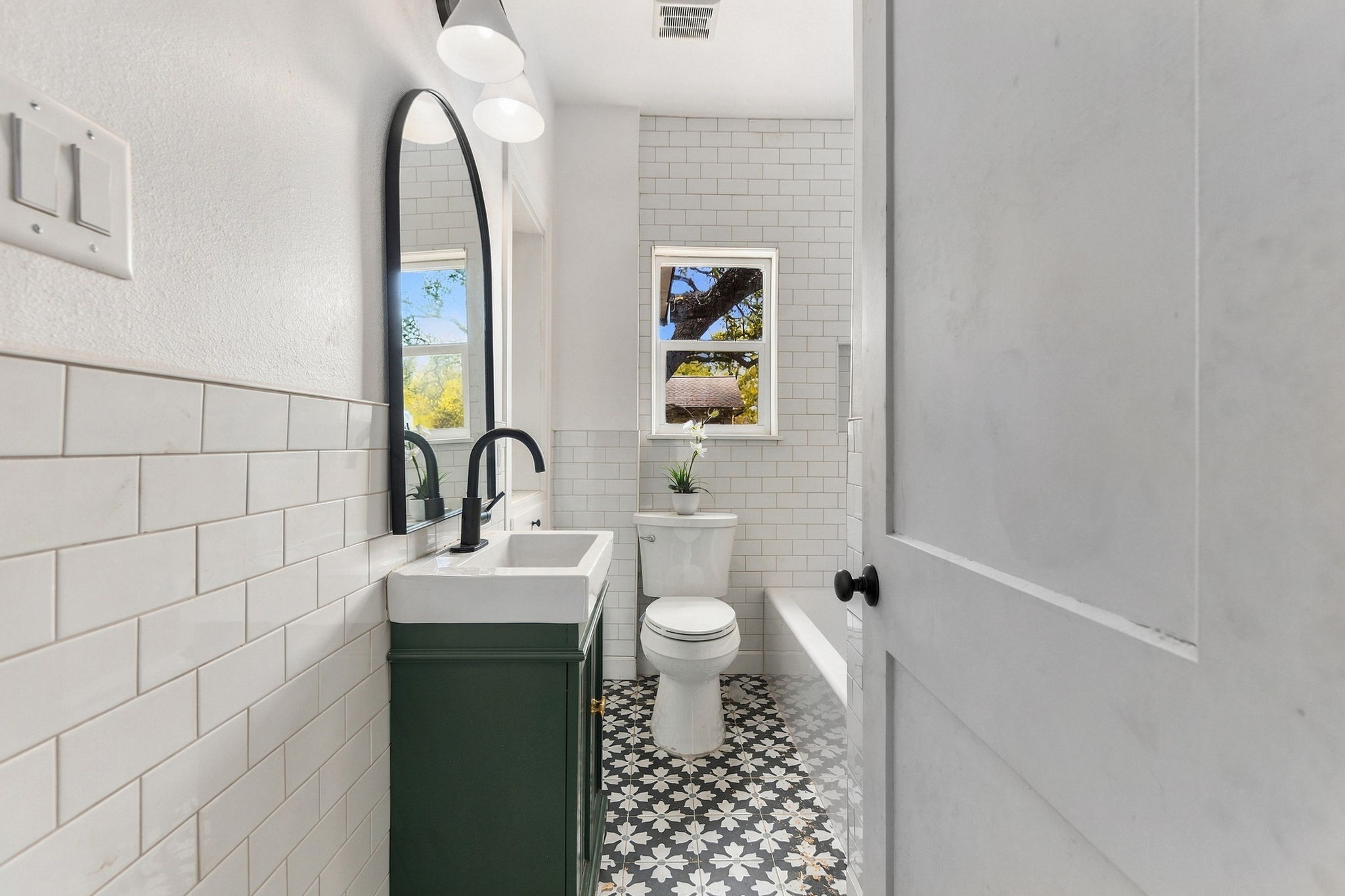 Bathroom with a deep green vanity, arched black mirror, subway tile and patterned floor tile