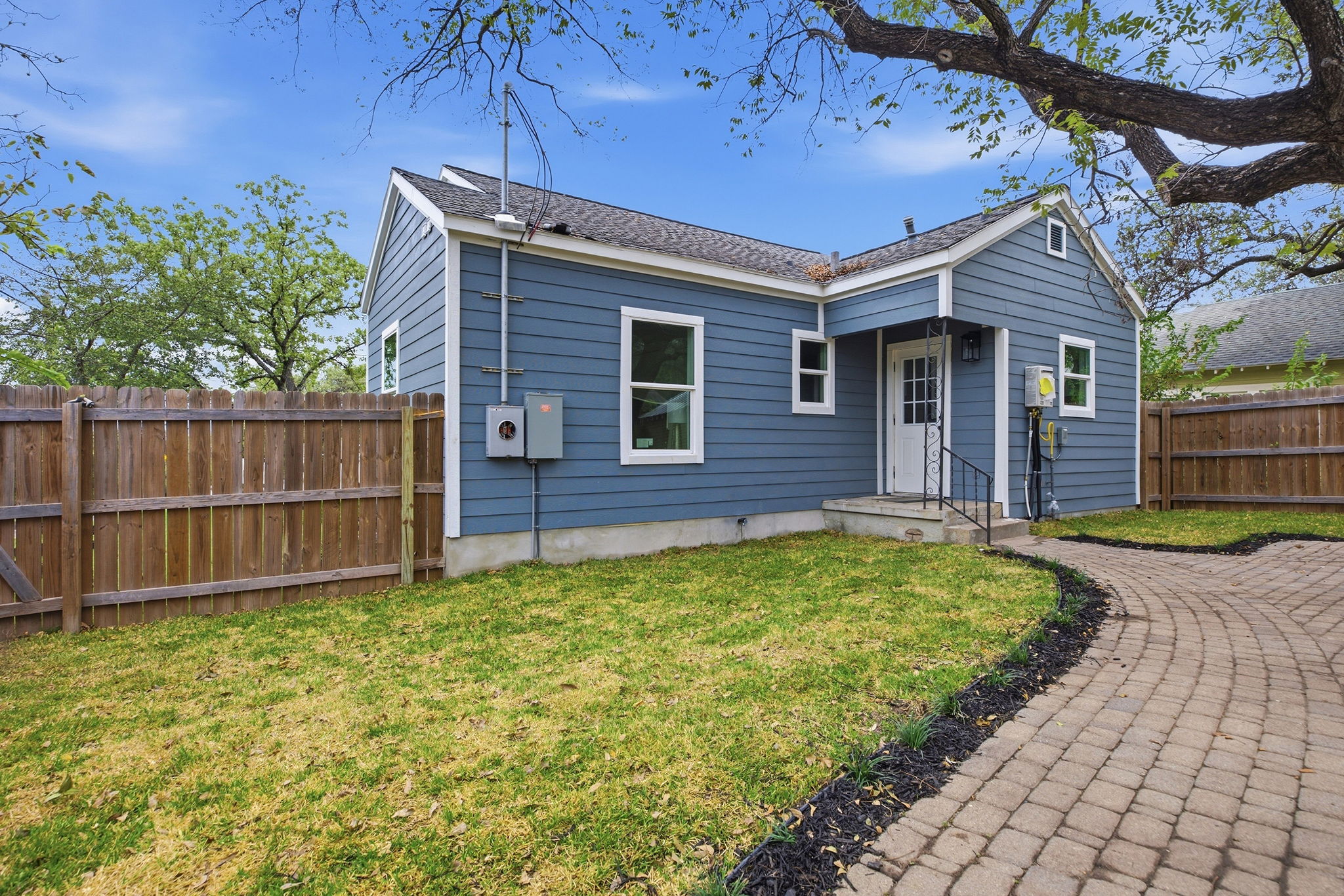Back of the home with a paver walkway and wood privacy fence