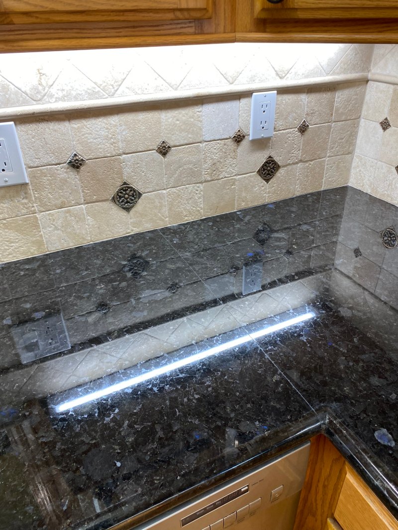 Black granite countertop and travertine backsplash before professional cleaning in South Bay CA