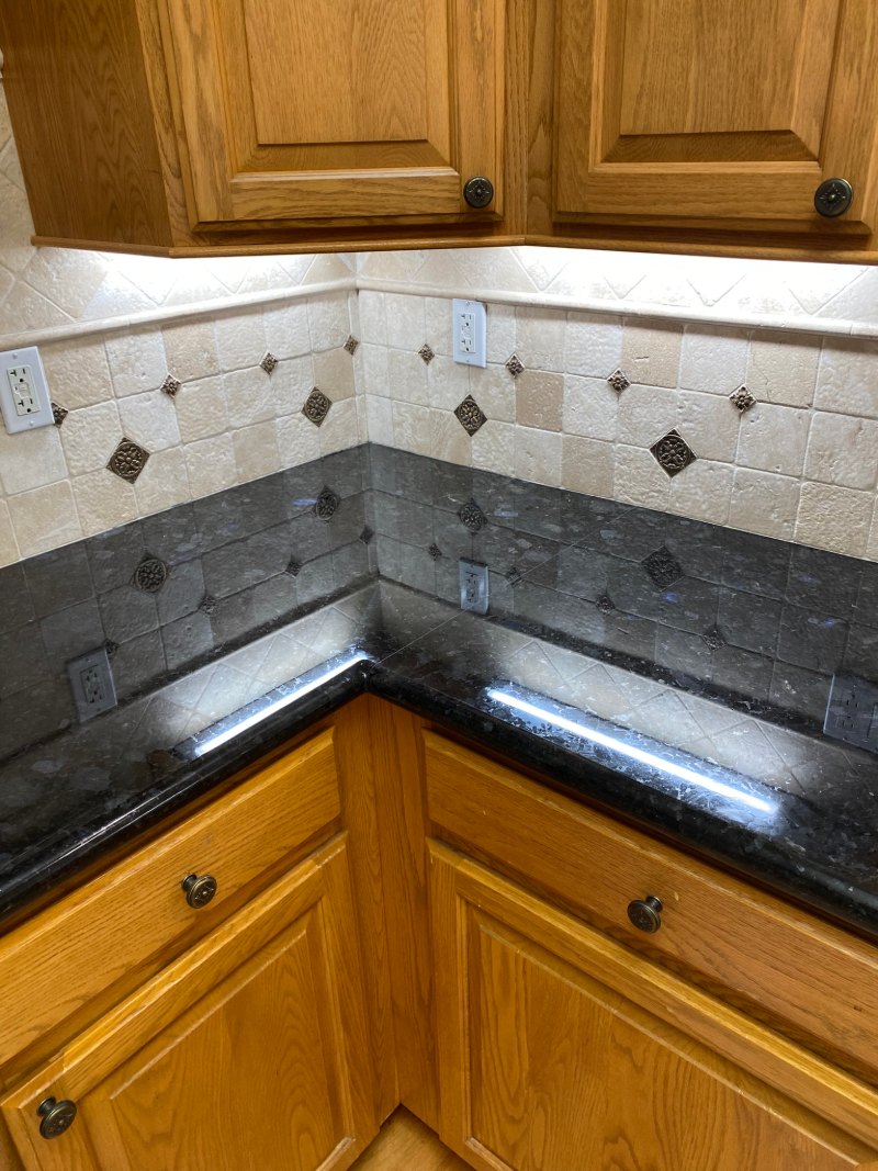 Black granite countertop and travertine backsplash after professional cleaning in South Bay CA