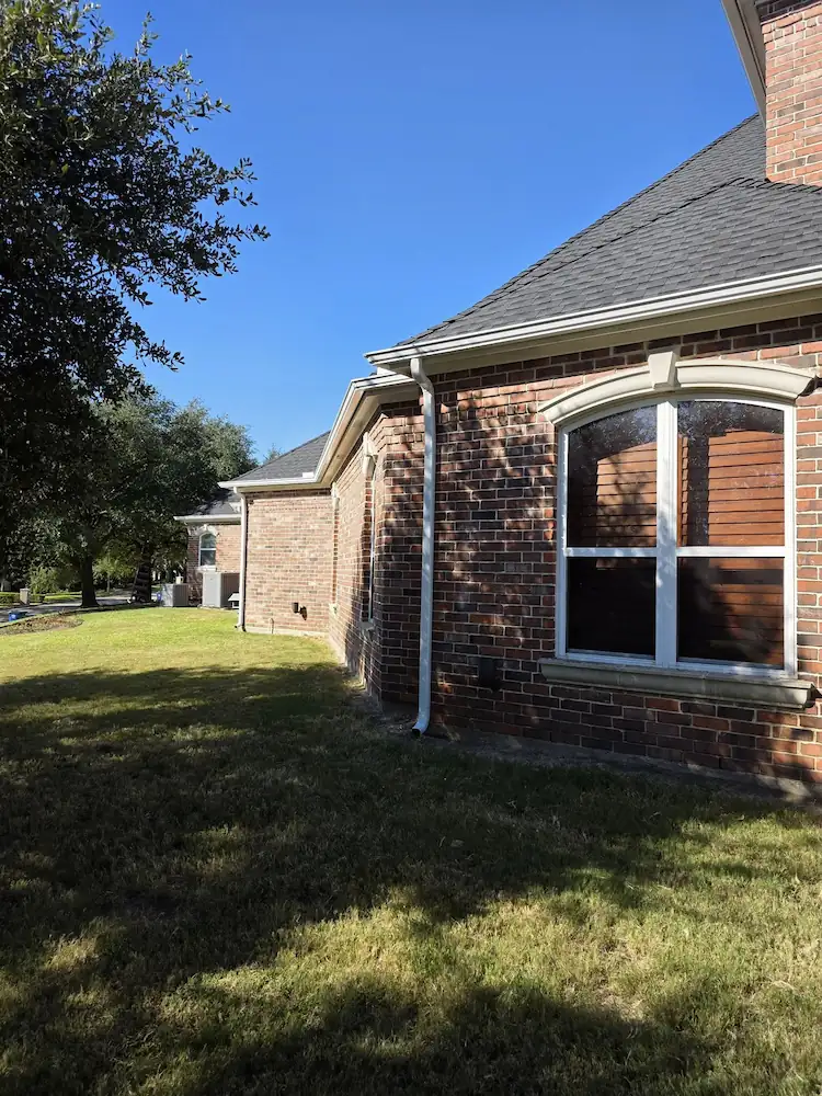 Brick home with a shingle roof and a gutter along the eave