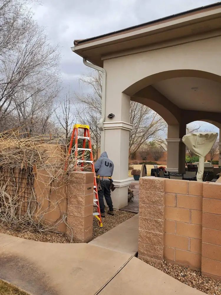 Crew member on a ladder beside an adobe-style wall and portal