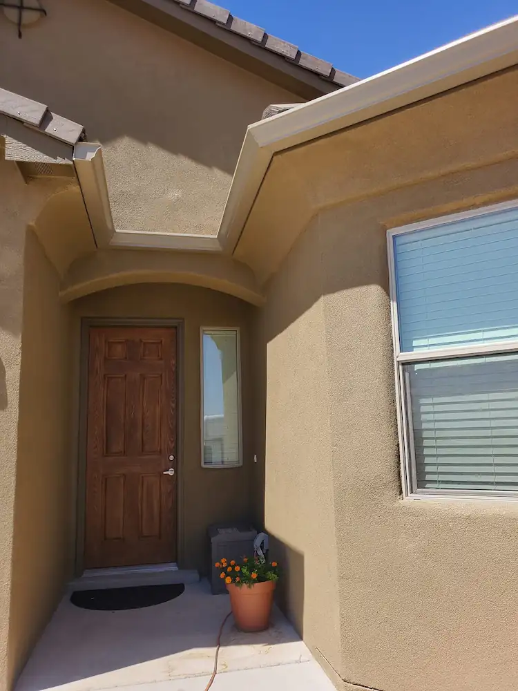 Stucco home entry with dark brown gutters along the roofline