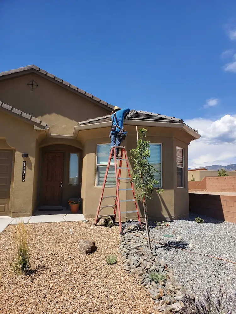 Stucco home with a ladder at the entry during gutter installation