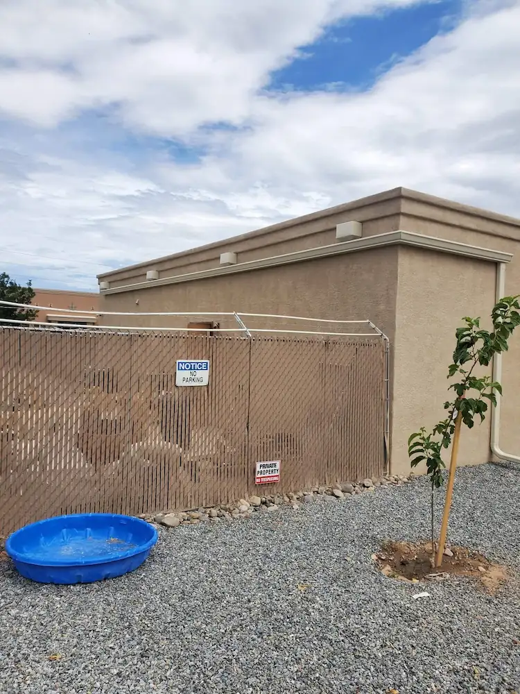 Tan stucco building with a parapet wall behind a wood fence