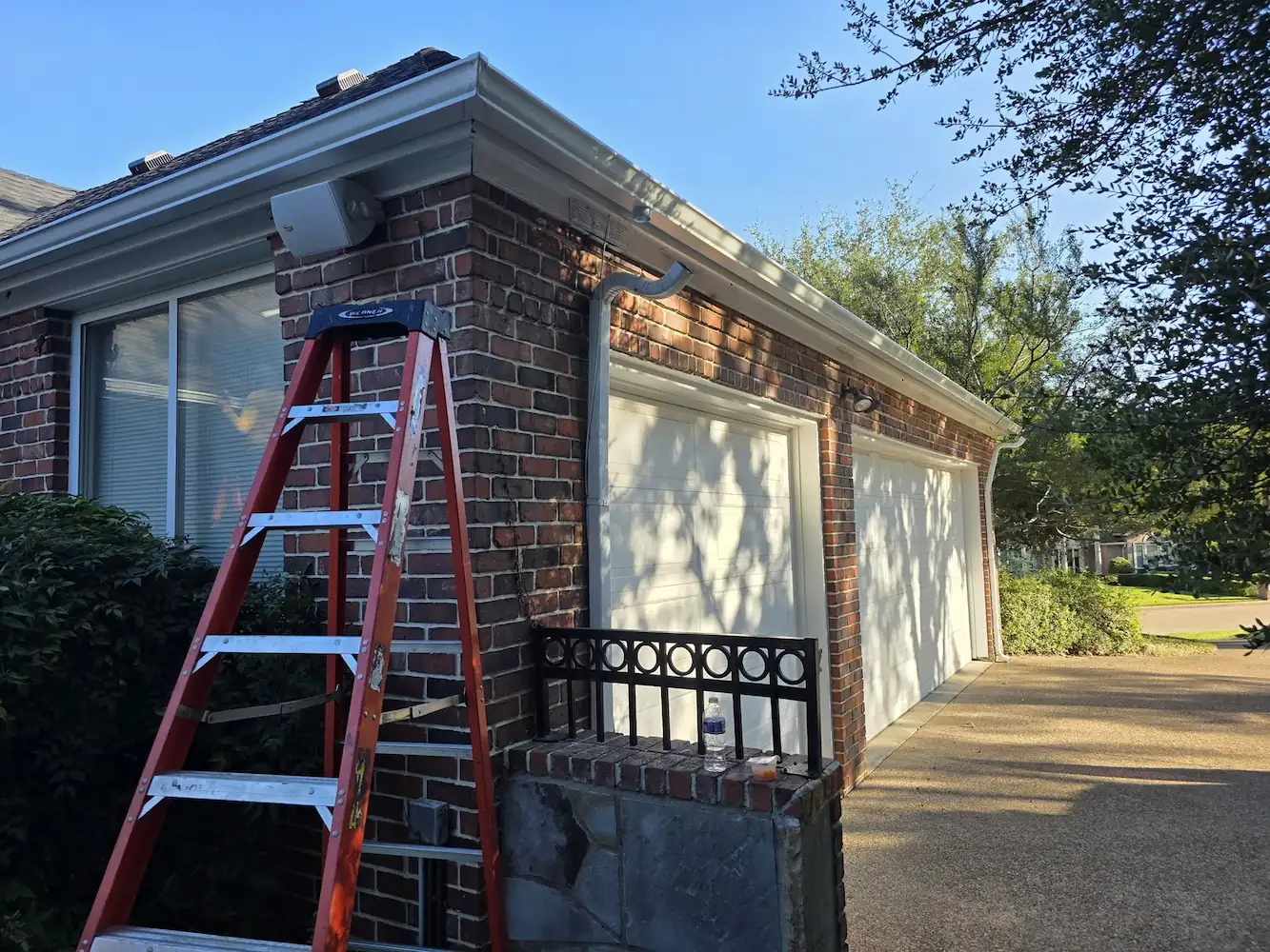 Red ladder set at a brick home entrance during gutter work