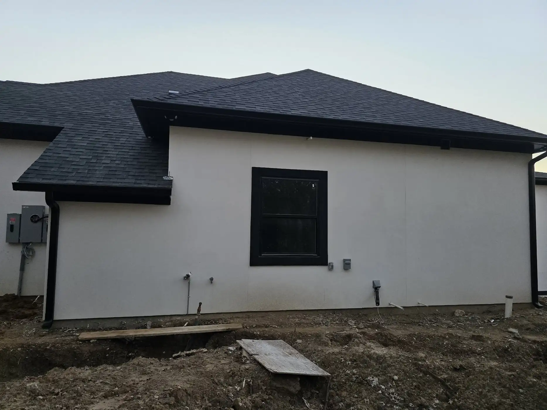 White stucco home with a dark shingle roof and a gutter along the eave