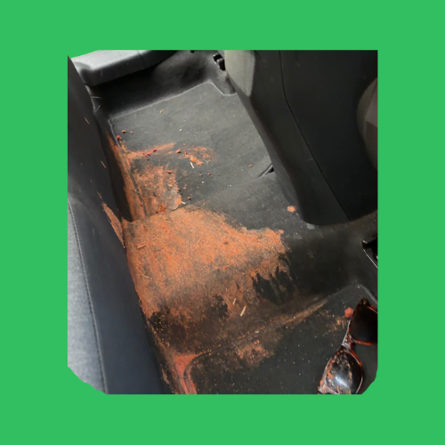 Stained car interior with red clay and spill damage before professional cleaning in Conestee SC