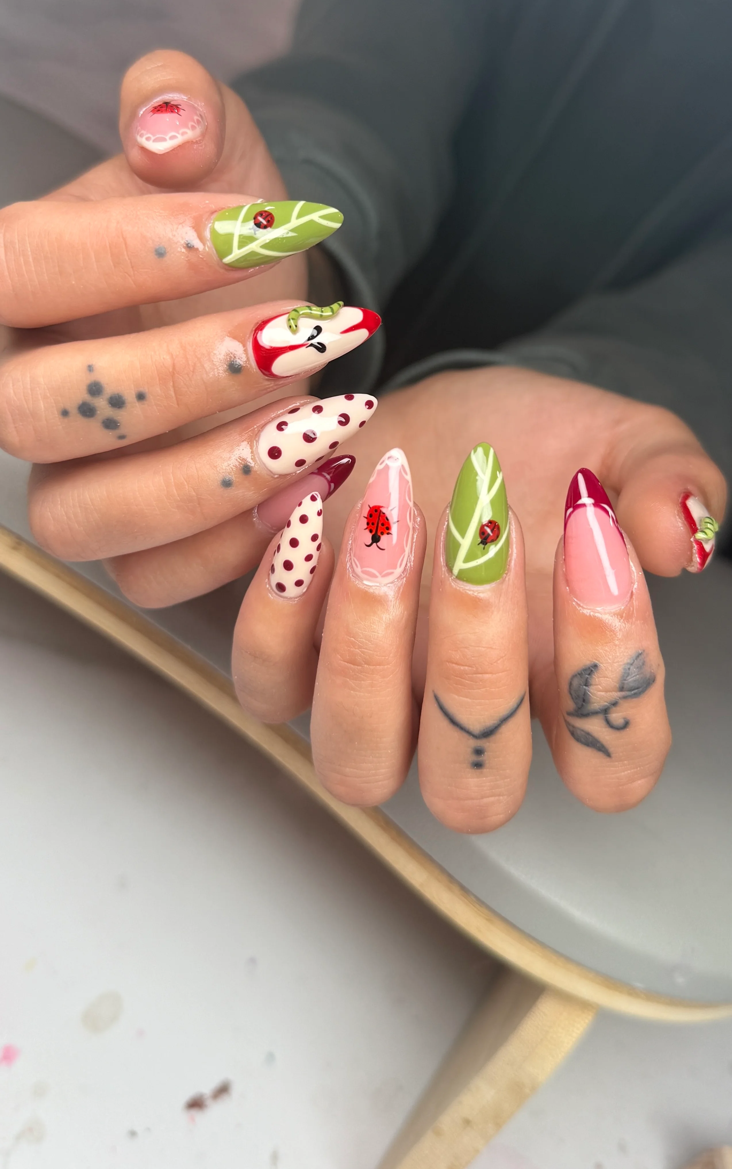 ladybug garden nail design with green leaf patterns, red accents, and polka dots by Ballerina Nails and Spa