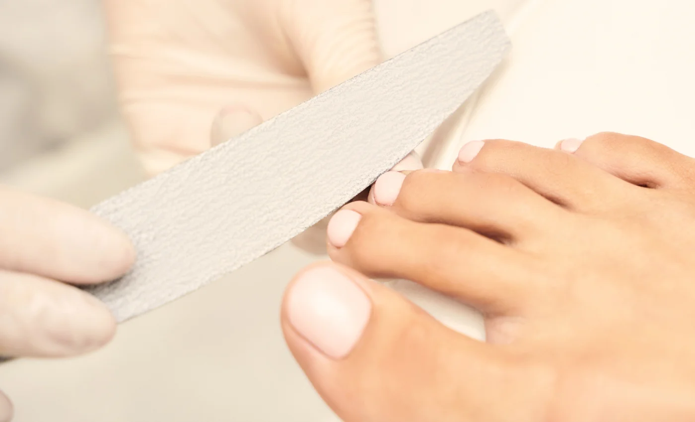 A nail technician performing a deep callus pedicure service