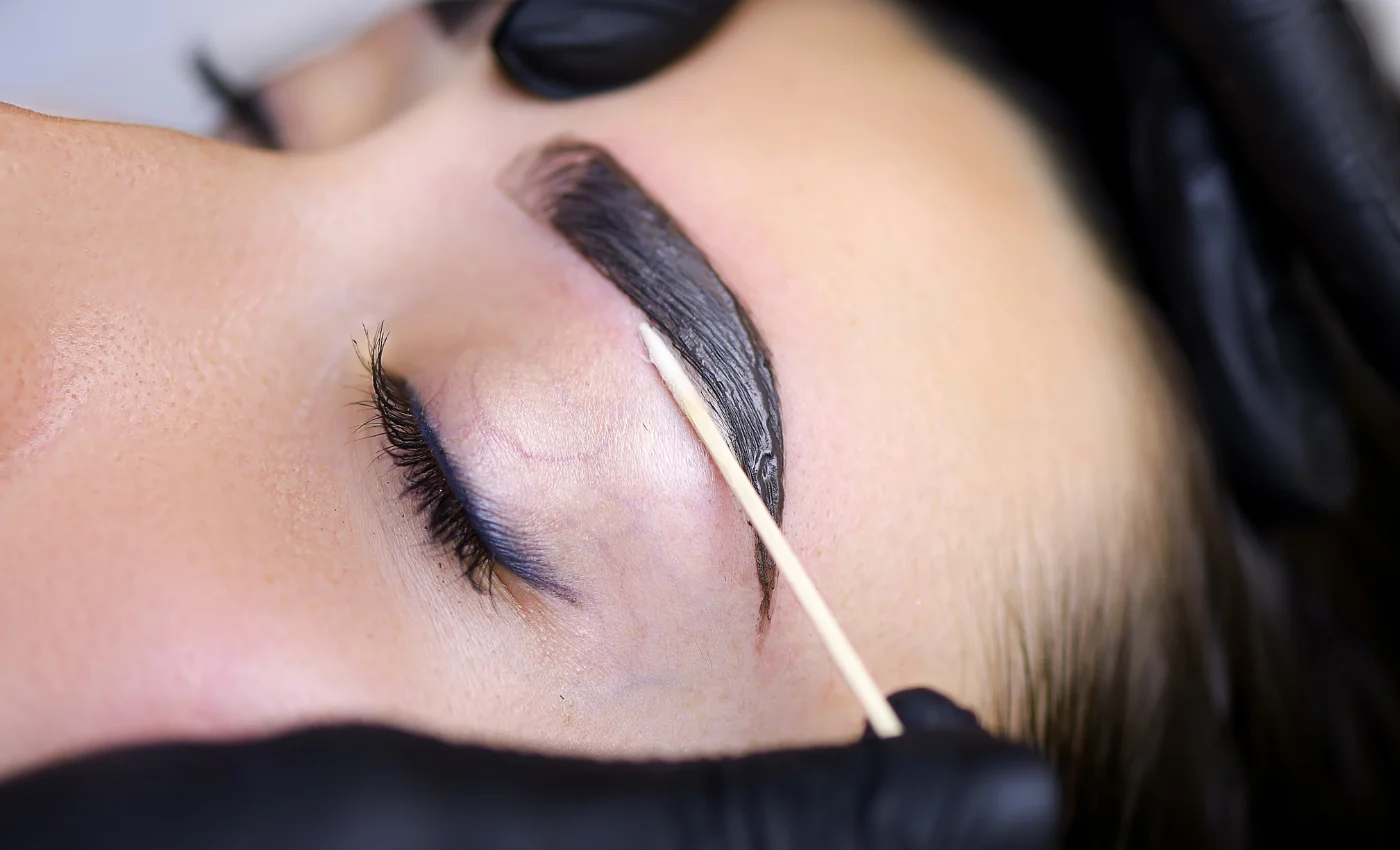 A technician applying brow tint for fuller-looking brows
