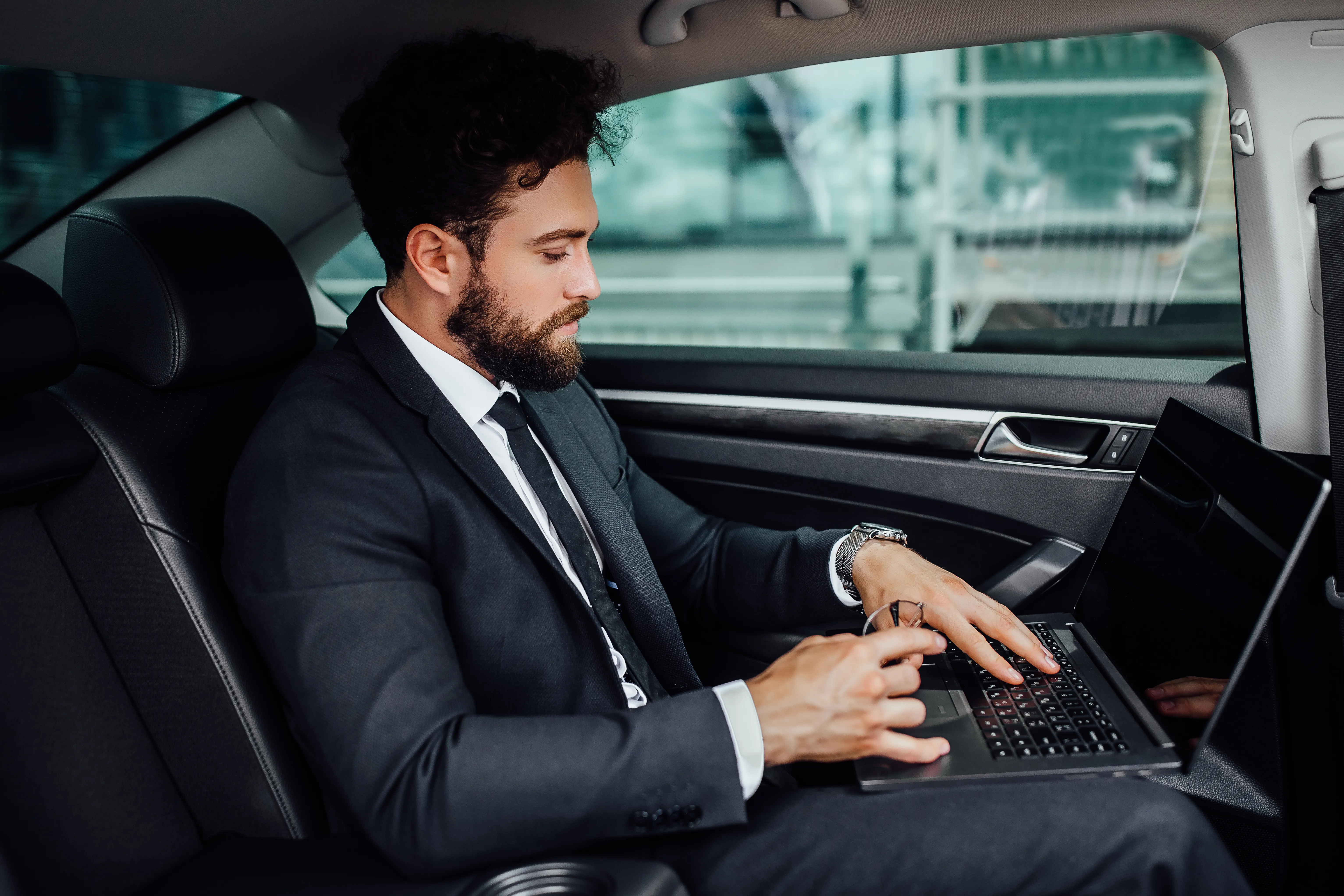 Executive working on a laptop in the back seat of a chauffeured car.