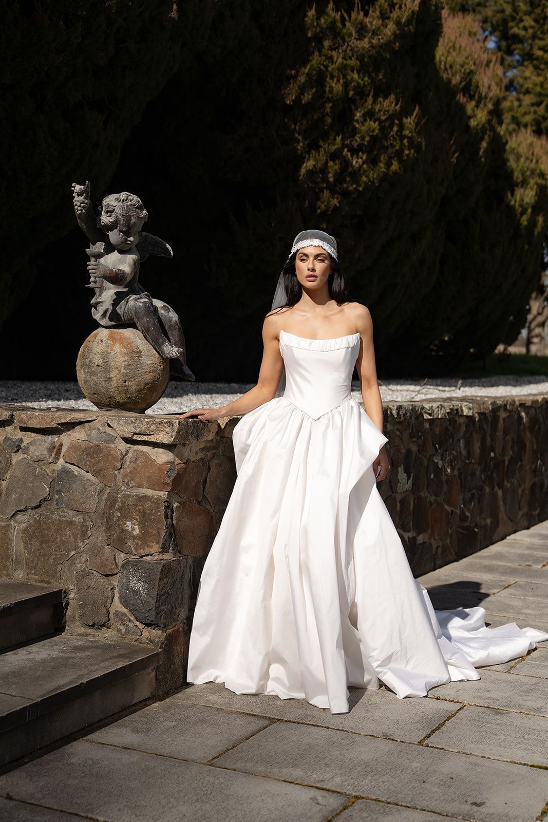 The Elodie, a strapless corset gown beside a stone statue