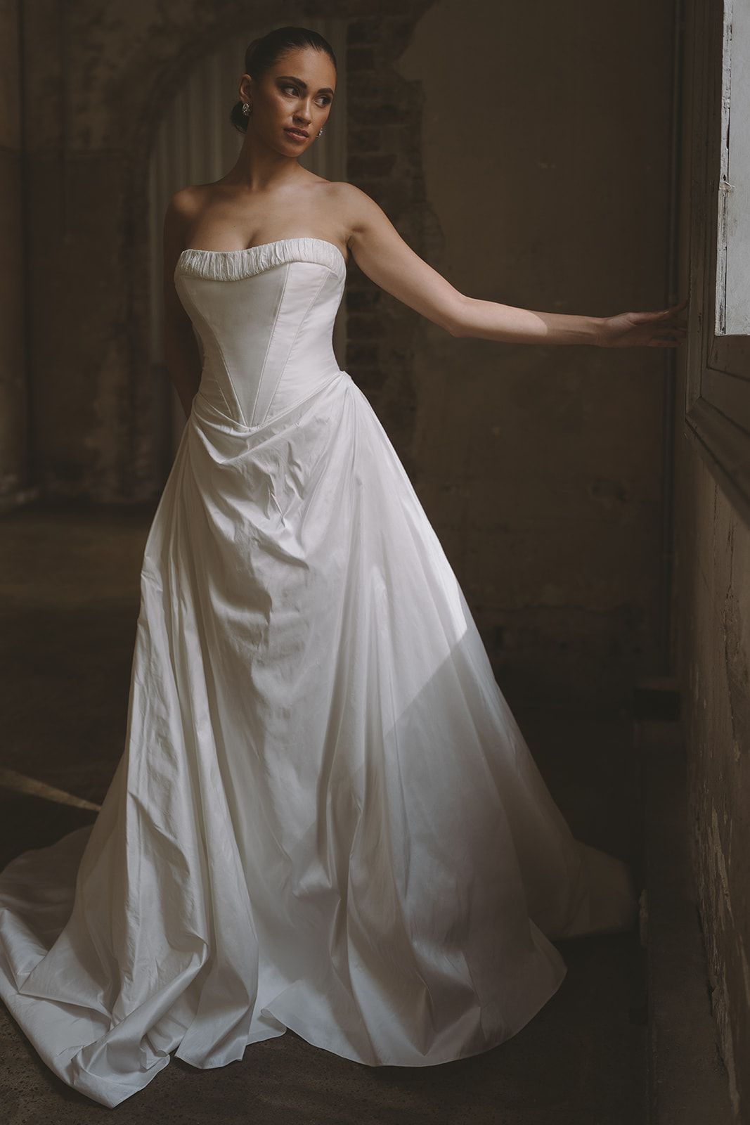 A bride in a strapless corseted Moira Hughes gown in soft window light