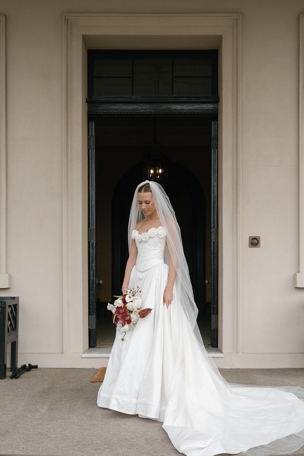 Real bride Molly in a rosette gown and long veil at the door of a heritage home