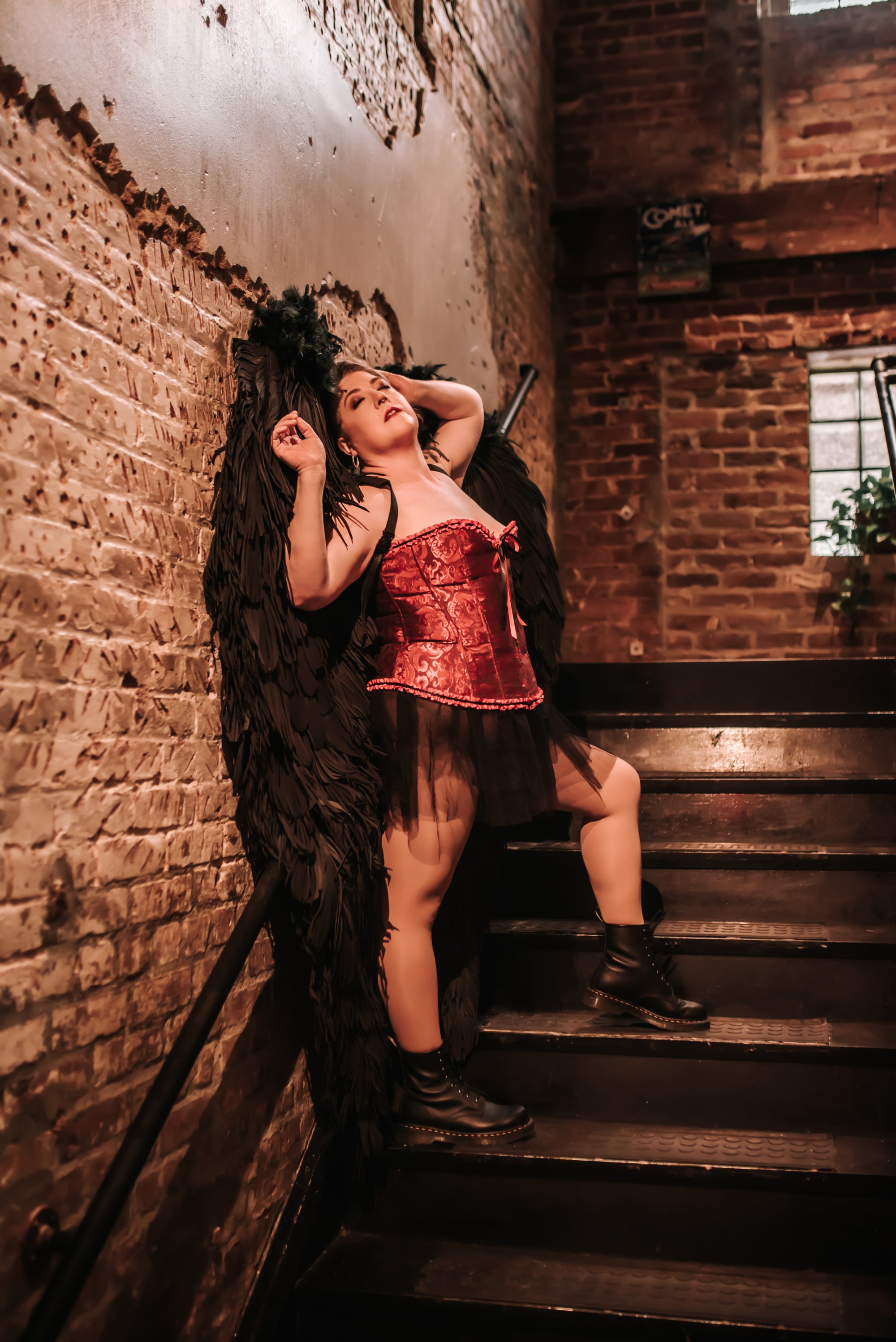 woman wearing red corset and black feather wings standing on staircase
