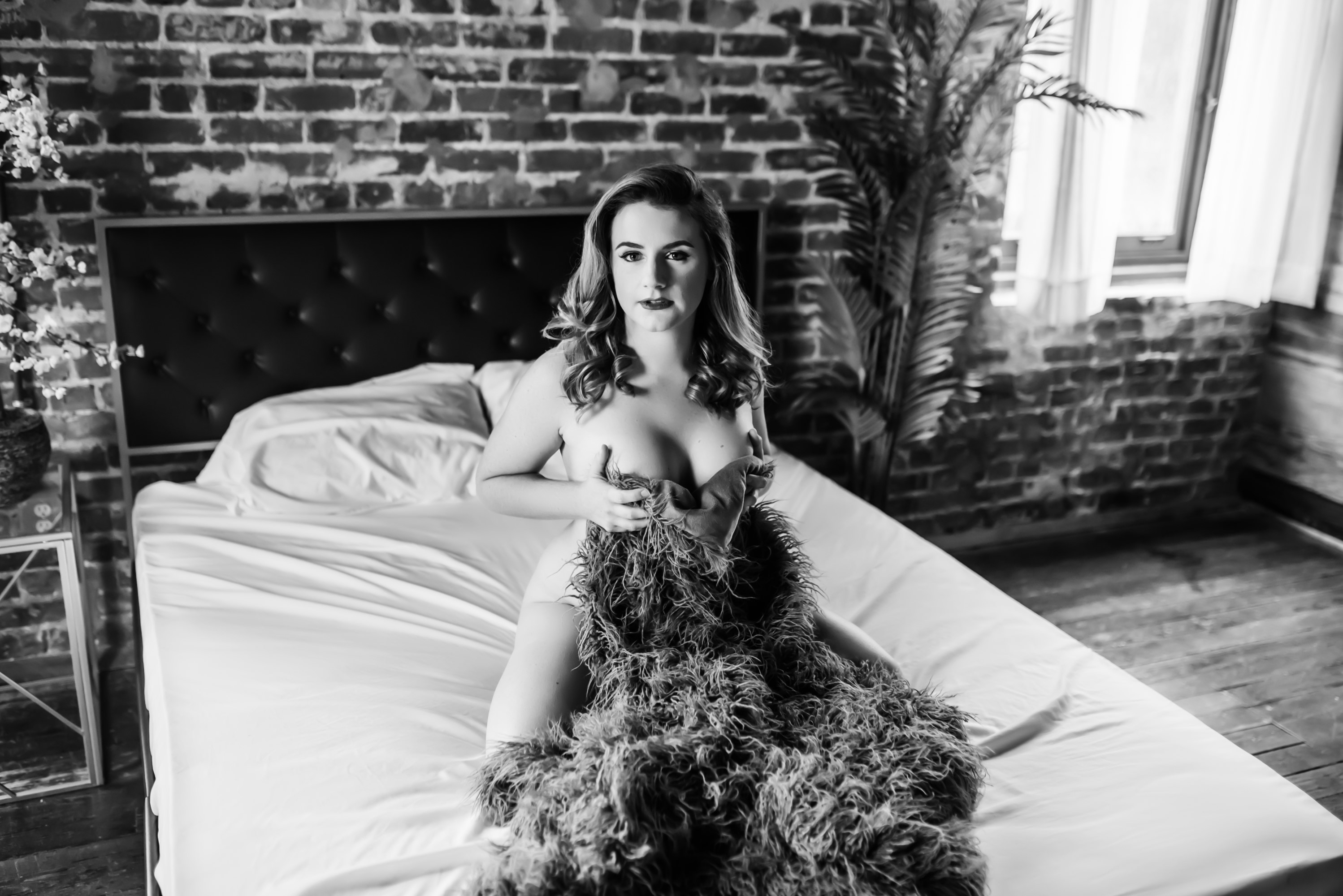 nude woman covering herself with fur blanket while kneeling on bed