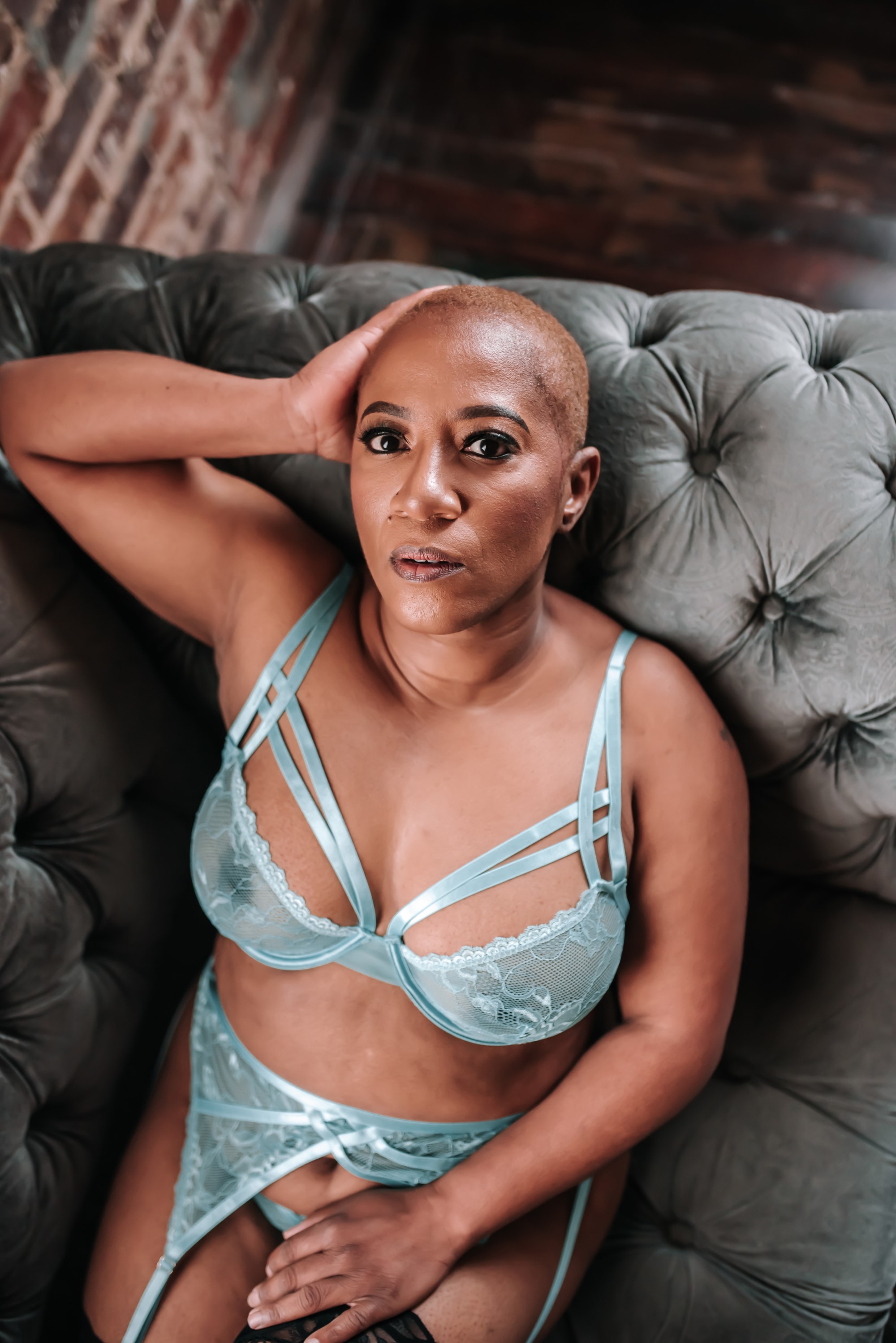 woman wearing light blue, see-through lingerie and lounging on grey couch