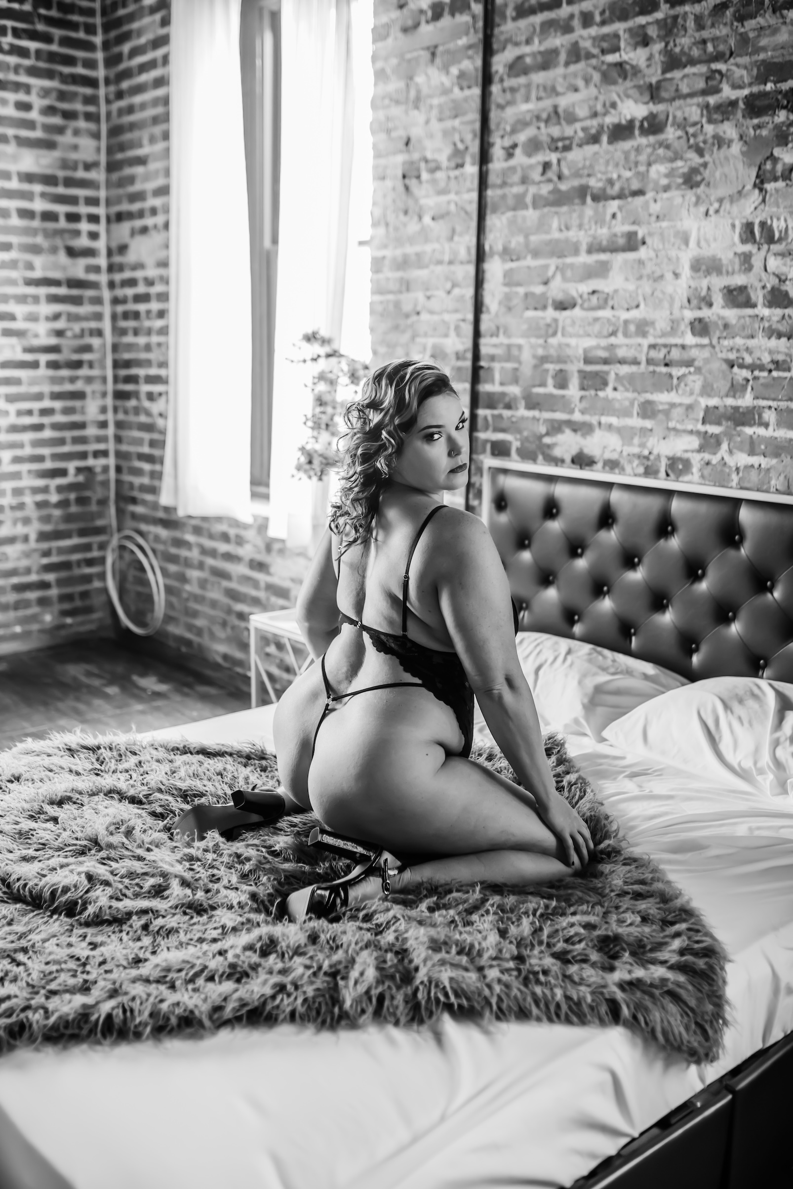 black and white photo of woman kneeling on bed while wearing lingerie