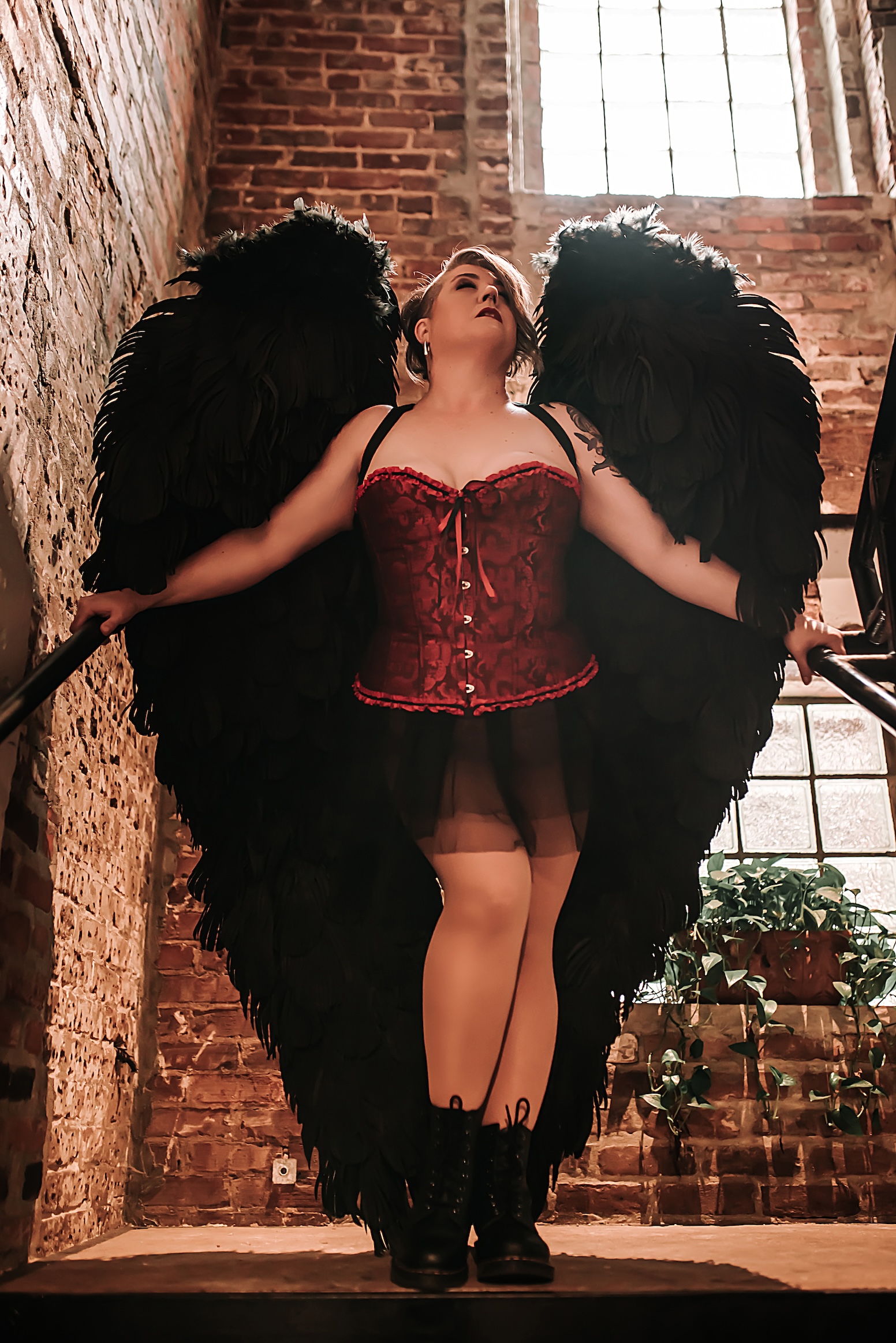 woman on staircase wearing red corset and black angel wings