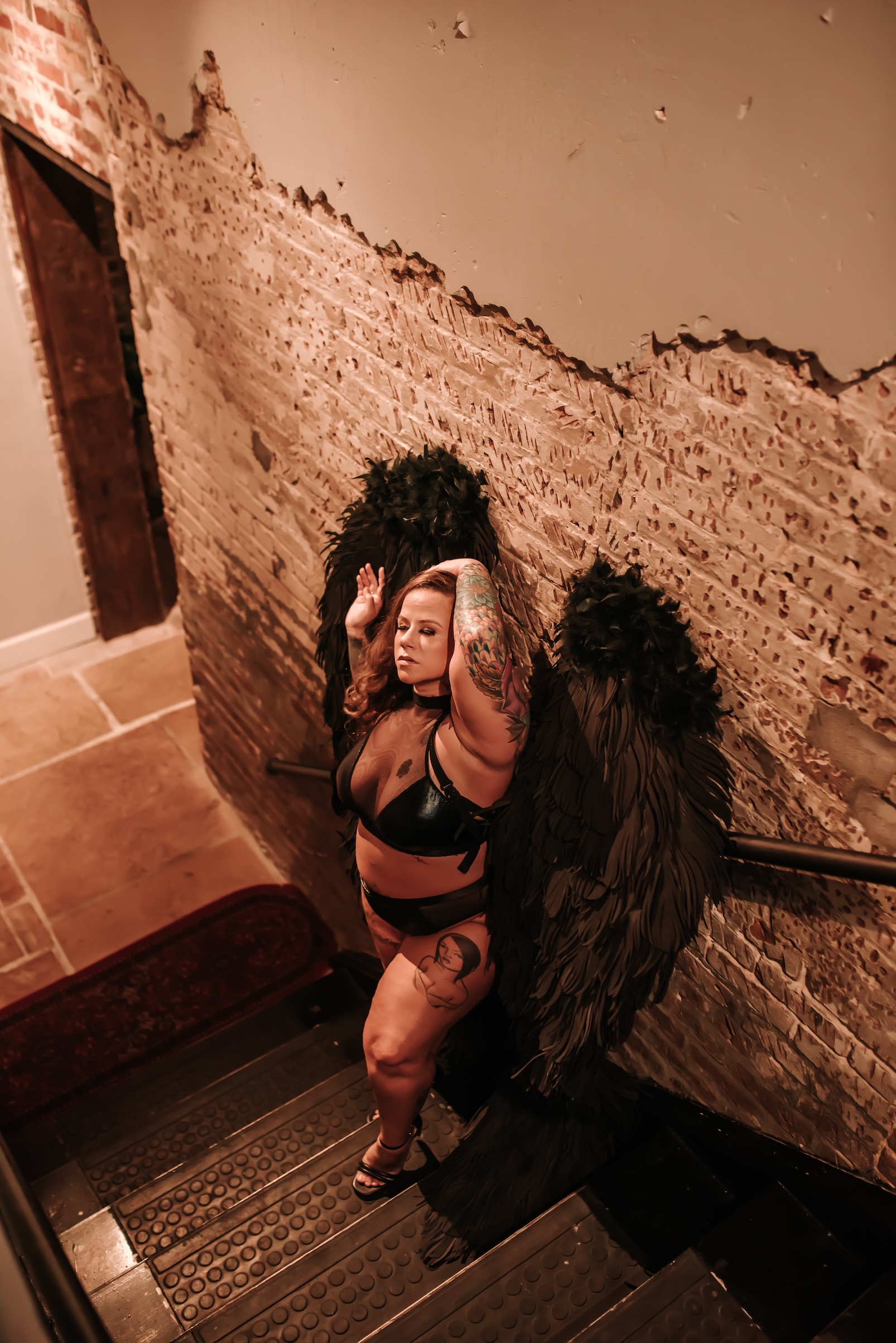 woman standing on staircase wearing black lingerie and black angel wings