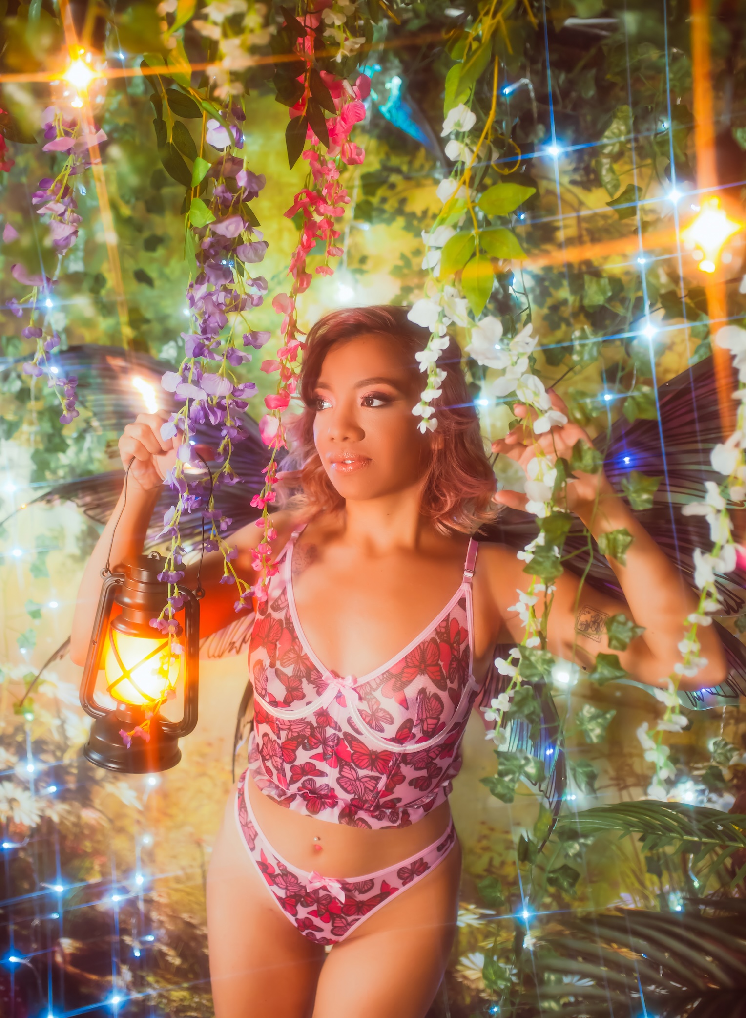 woman in fairy wings and butterfly lingerie standing amongst vines and fairy lights