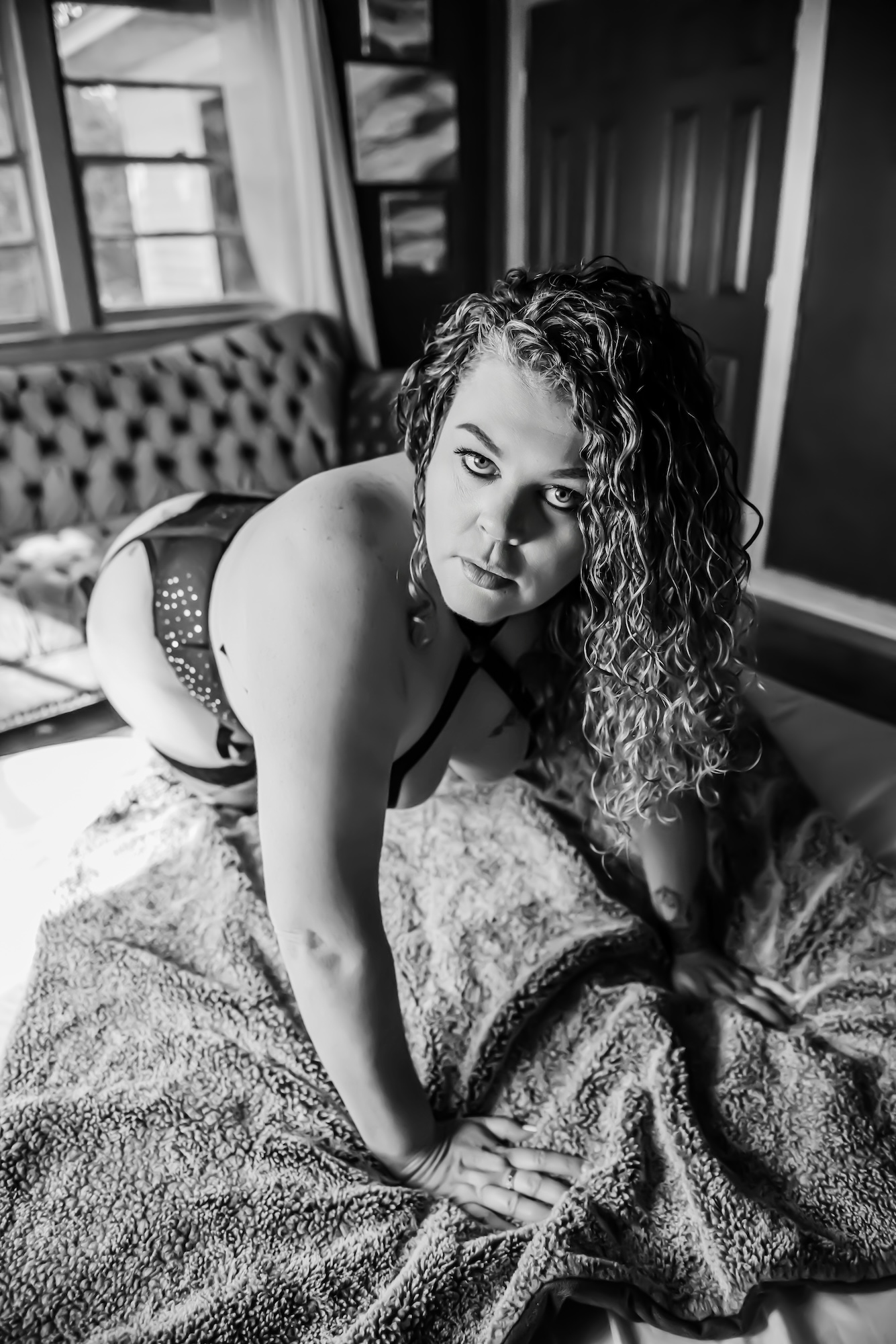 black and white photo of woman kneeling on bed while wearing lingerie