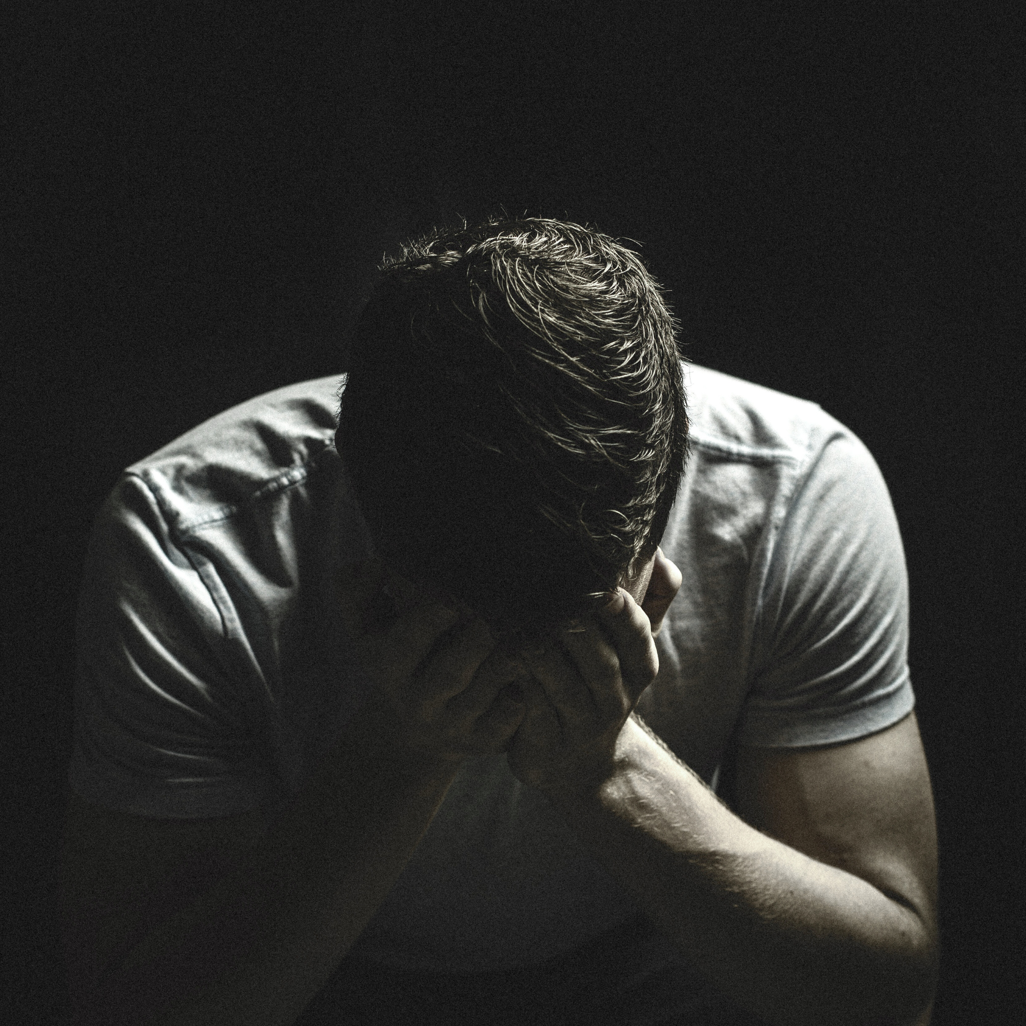Man in shadow holding head in his hands, representing shame reversal, emotional healing, and resilience coaching with Adam Feuerstein