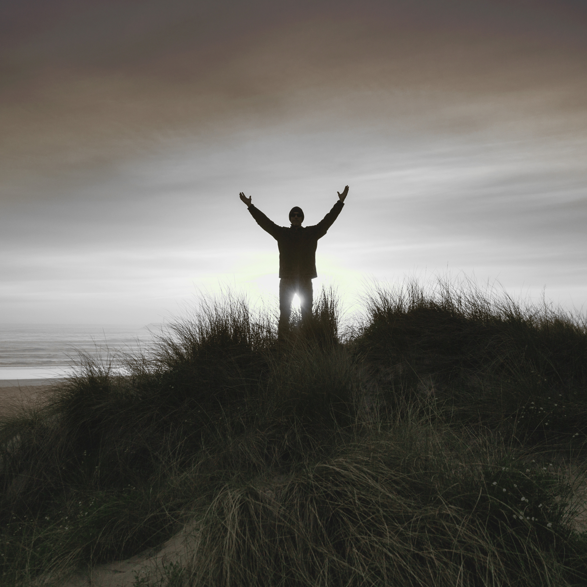 Man standing on coastal dunes with arms raised in freedom, symbolizing self-leadership and empowerment through Adam Feuerstein’s coaching