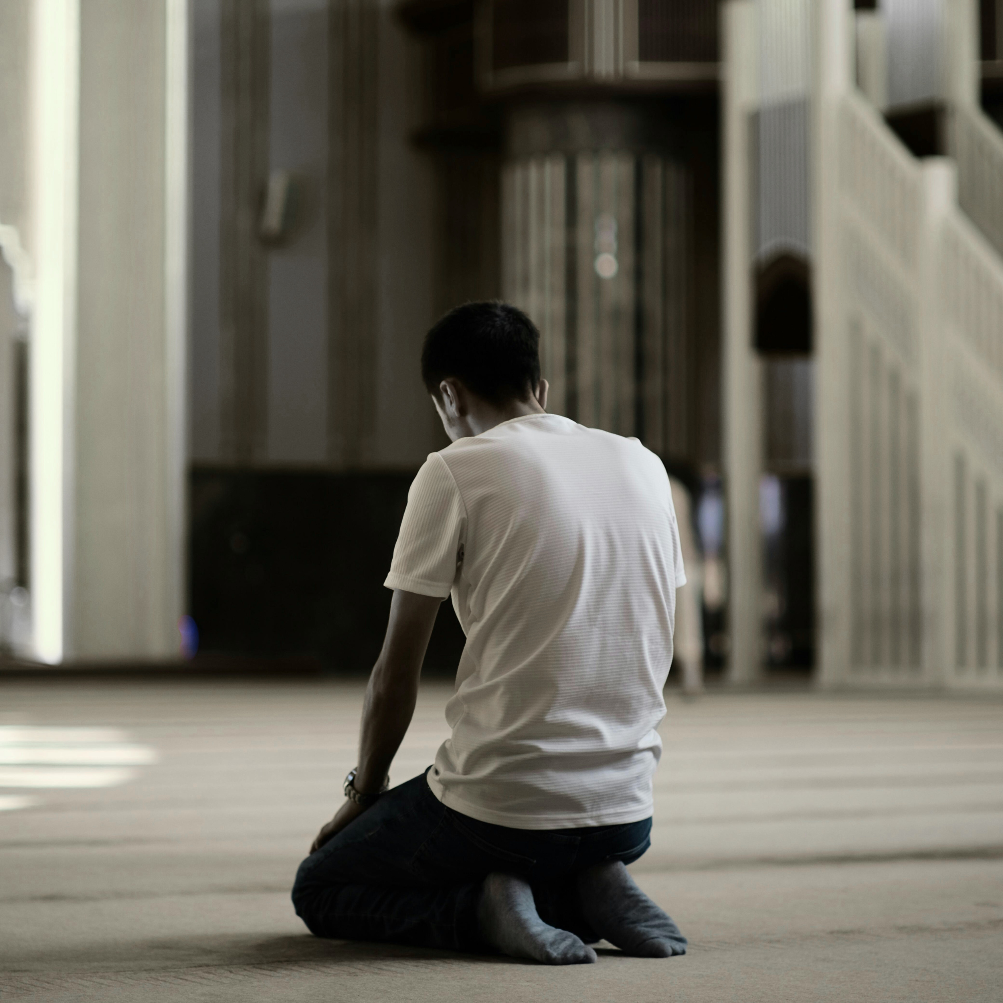 Man kneeling in reflection inside a wide space, symbolizing spiritual rewilding, deep connection, and personal transformation with Adam Feuerstein