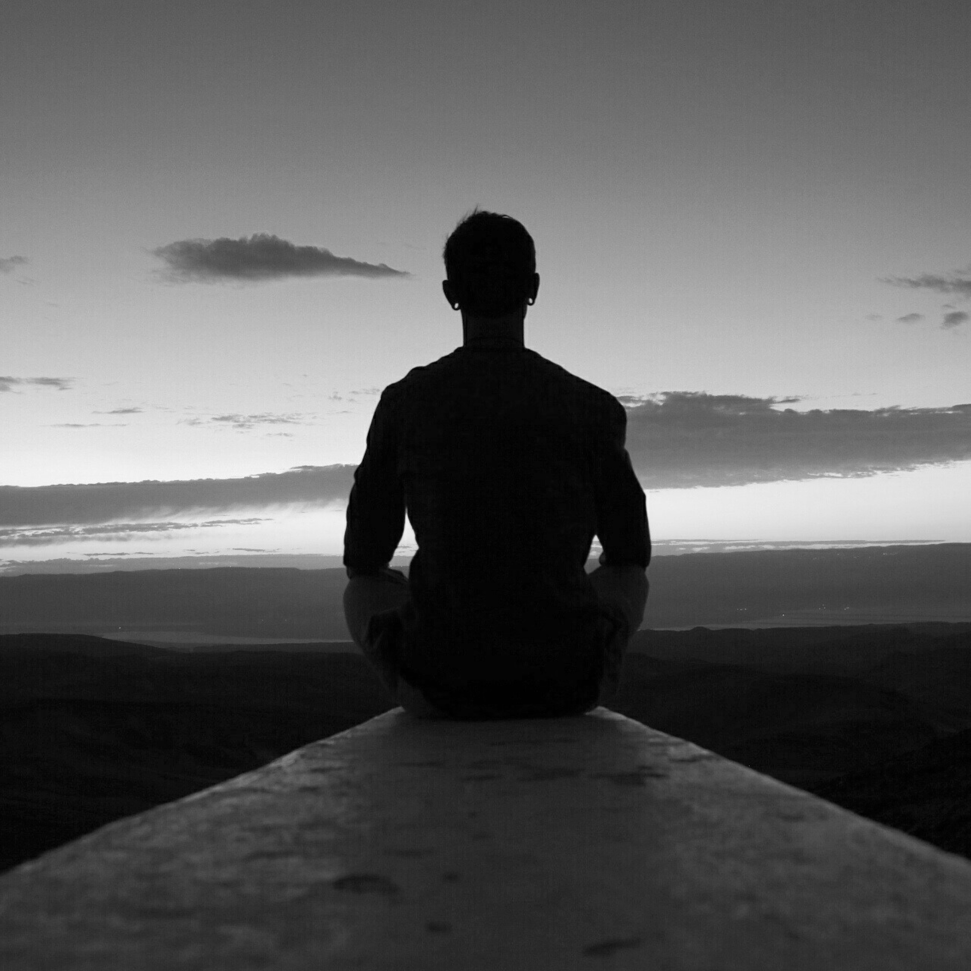 Silhouette of man meditating at sunset on mountain ridge, representing daily rituals, embodied practices, and mindful leadership with Adam Feuerstein