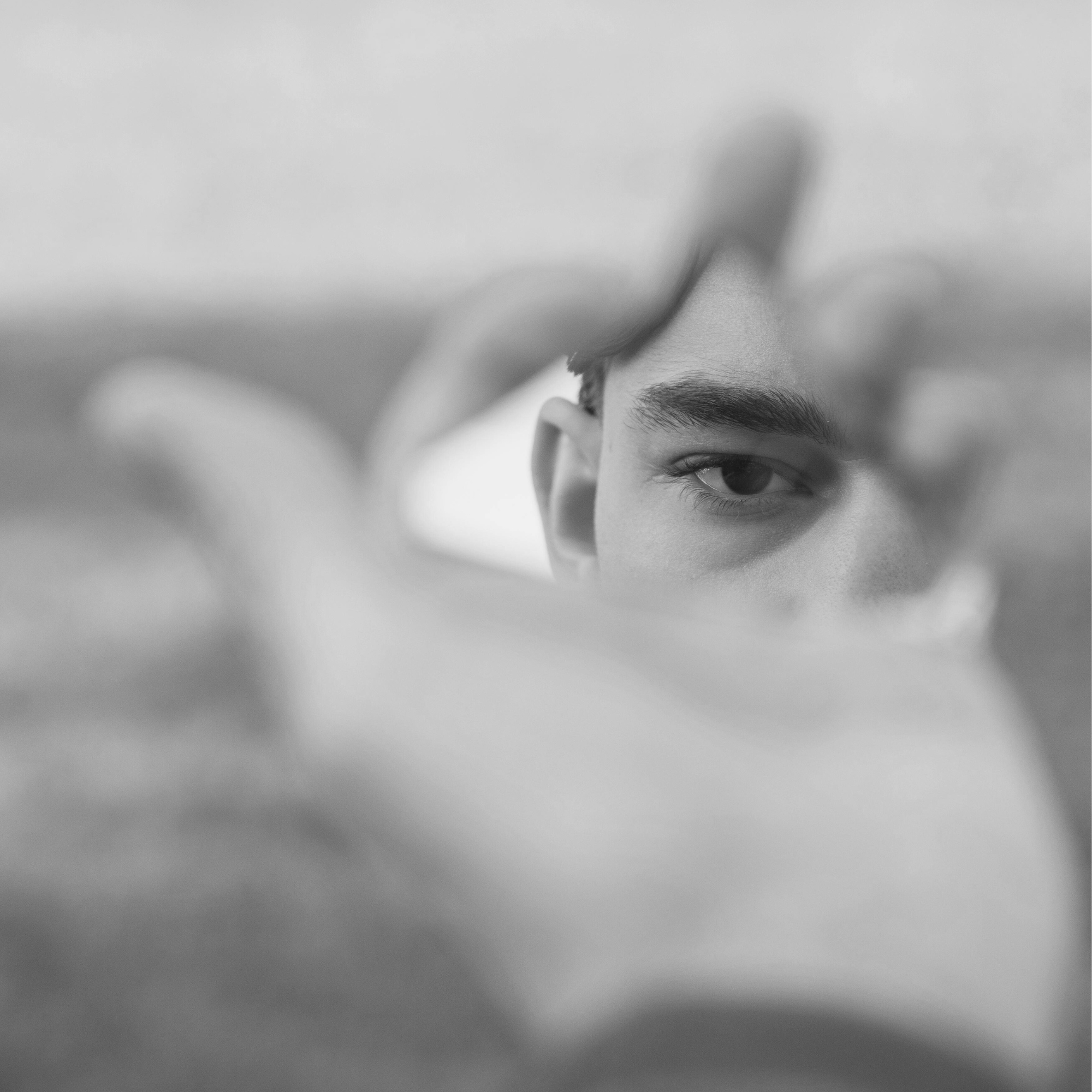 Black and white portrait of a man framed by his hand, symbolizing self-reflection and reclaiming identity. Represents Adam Feuerstein’s coaching for breaking free of societal roles, embracing sacred connection, and leading with authenticity