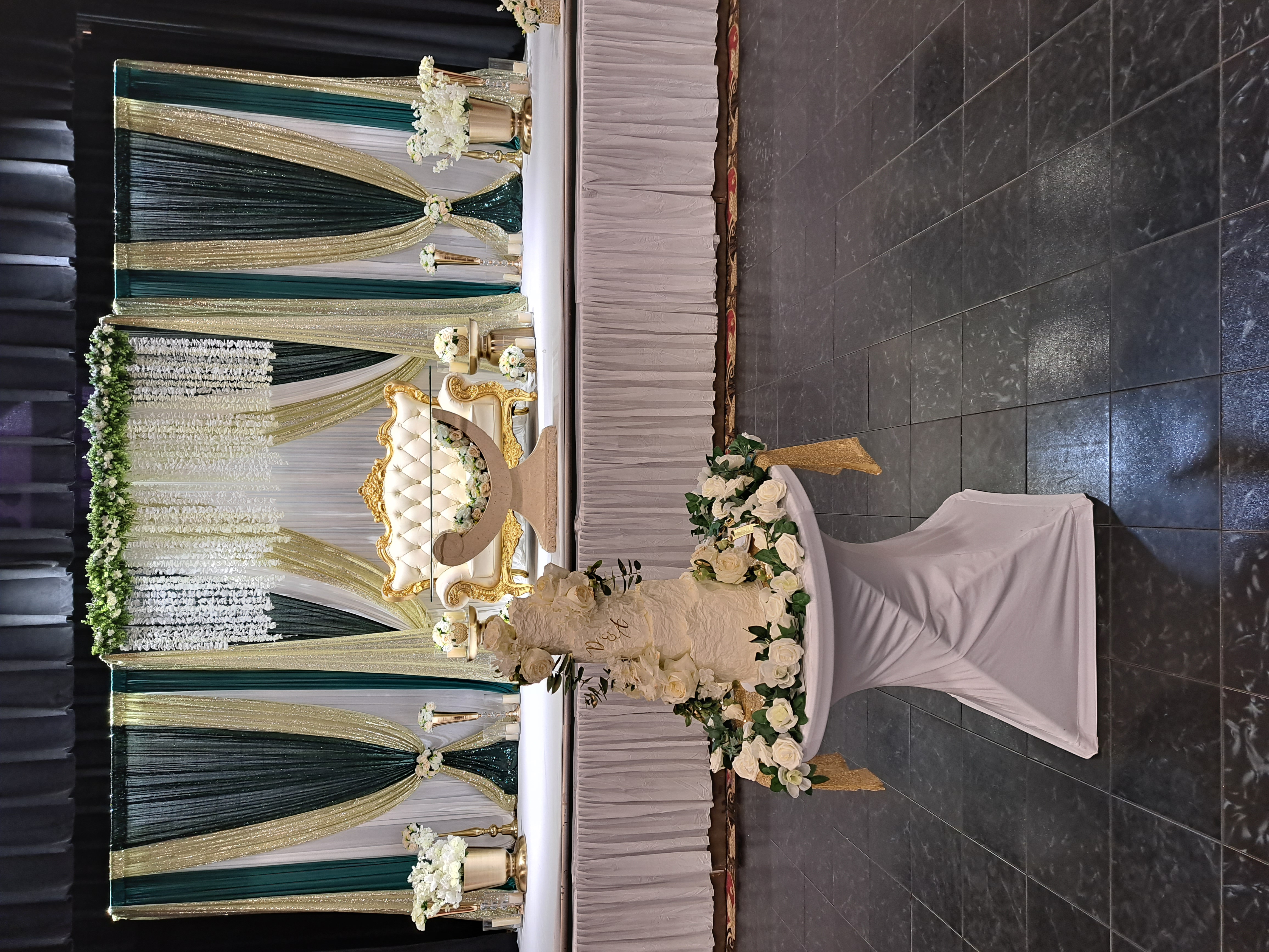 A tiered wedding cake on a draped table in front of a teal and white stage