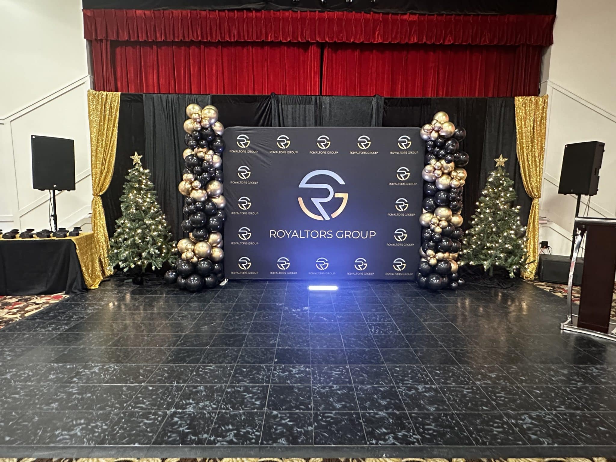 A branded corporate backdrop flanked by decorated Christmas trees on the ACCA stage