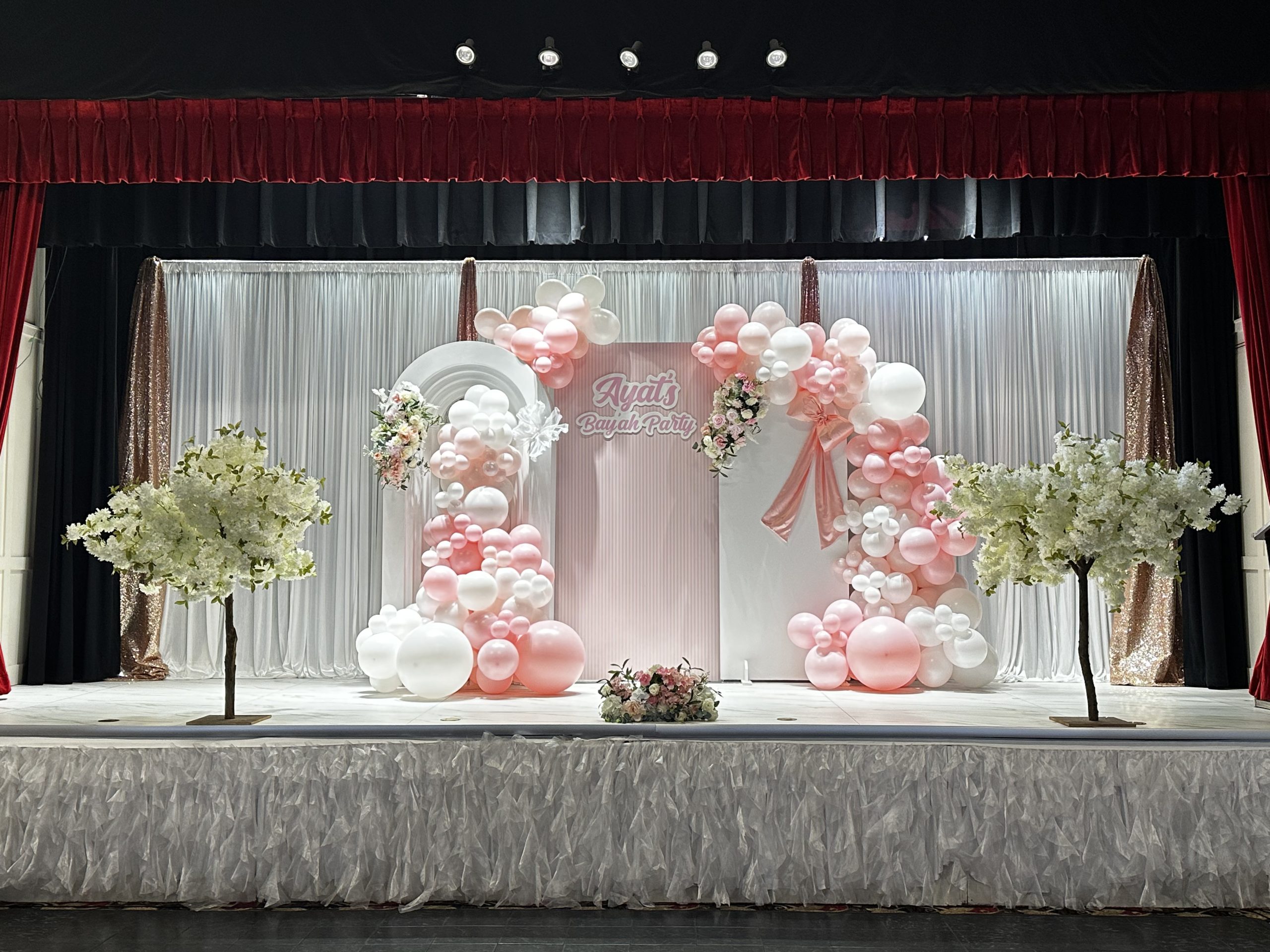 A blush and white stage with a balloon and floral arch behind the head table