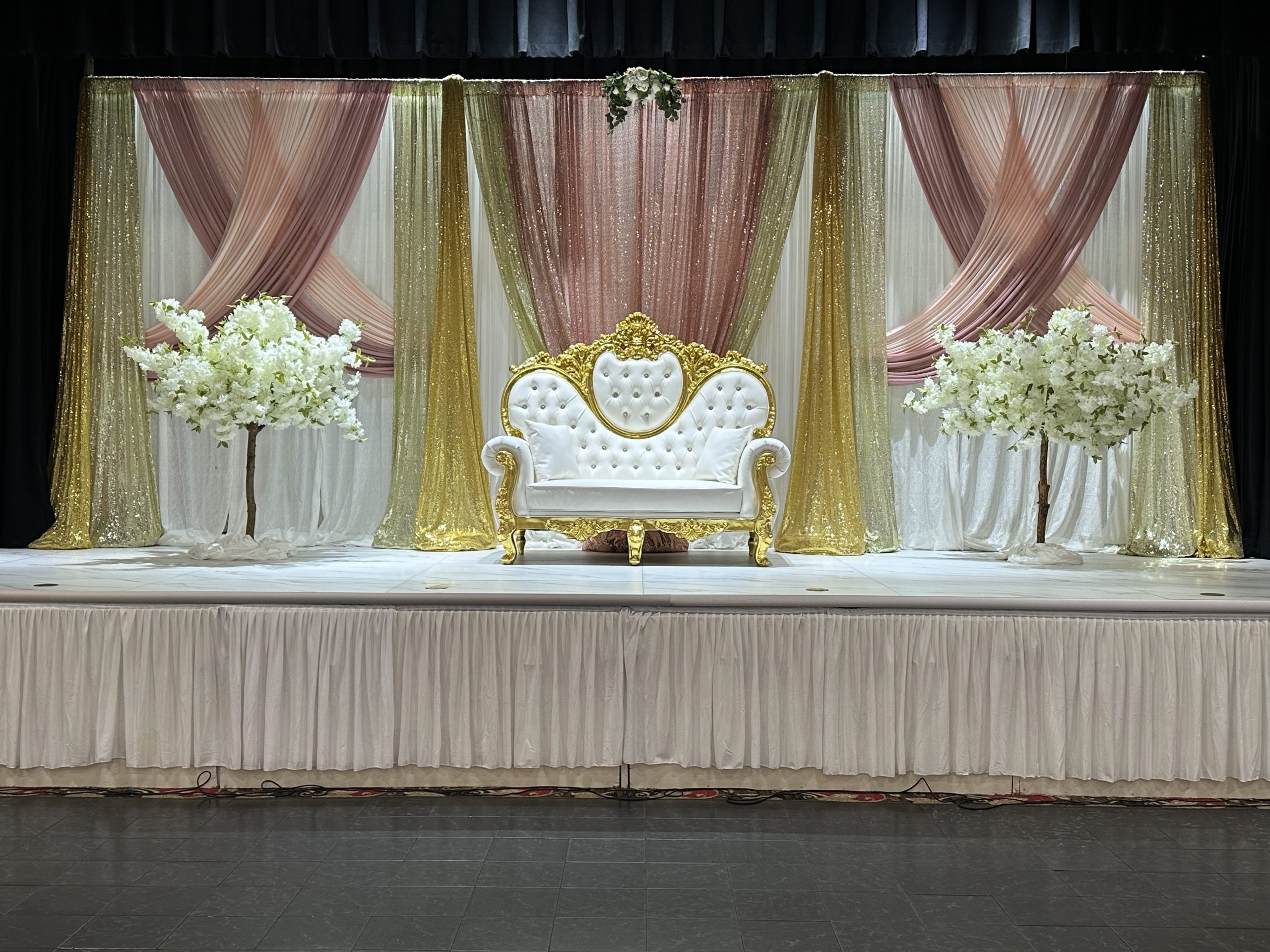A pastel pink and gold draped stage with a cream settee