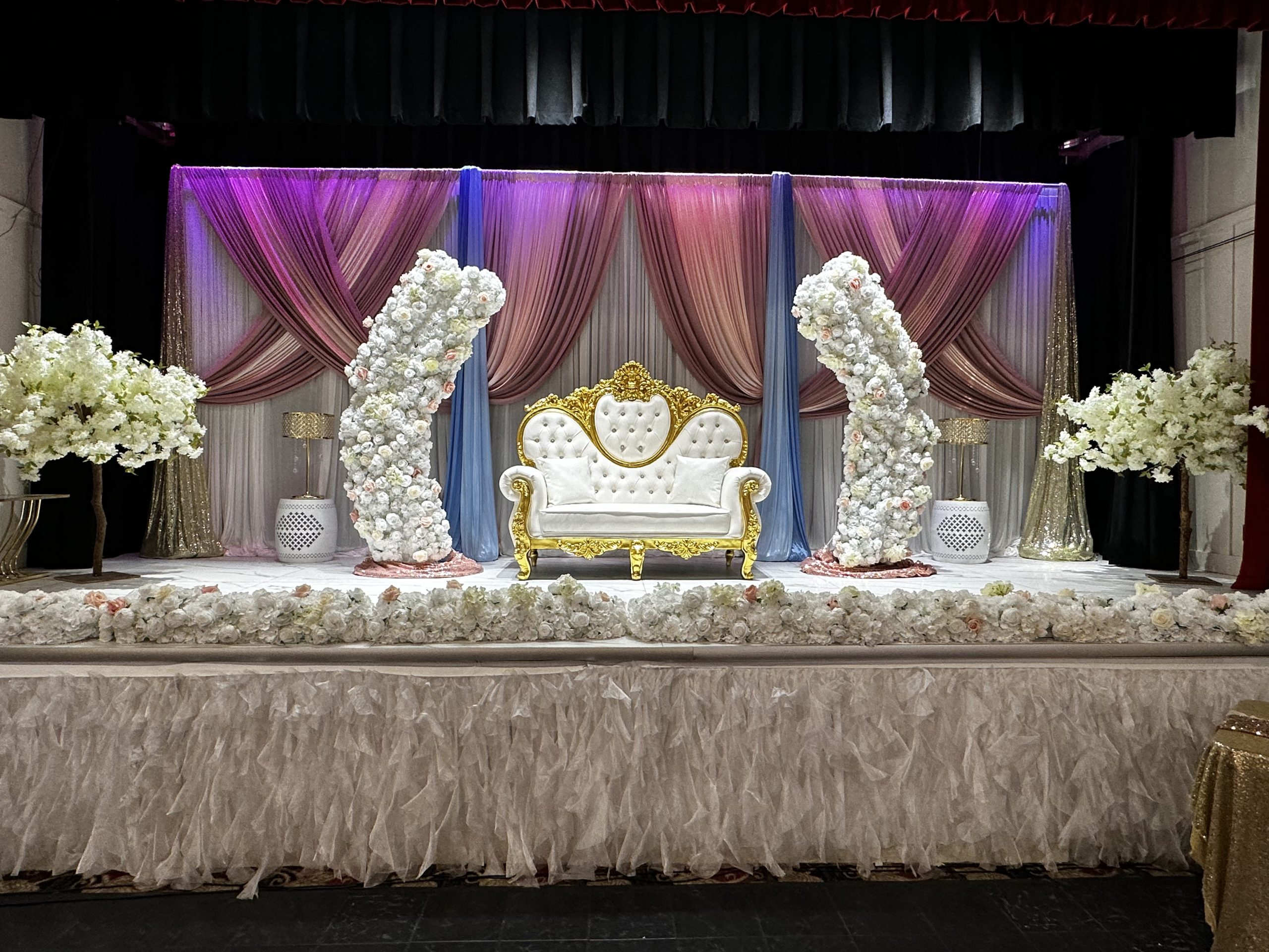 A purple and gold stage with twin throne chairs and floral columns