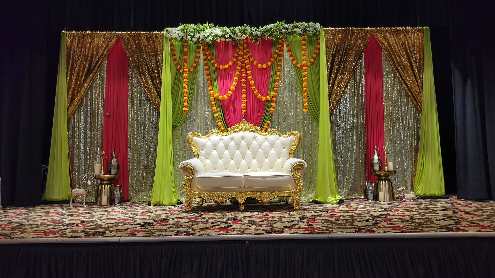 A green, yellow and pink draped stage set for a cultural ceremony