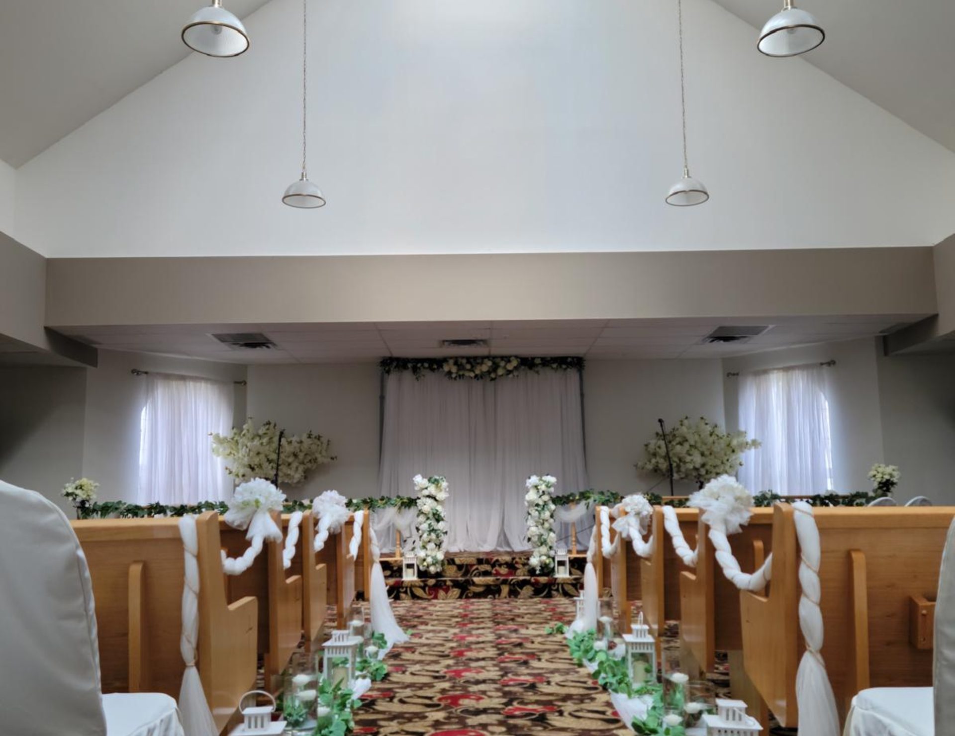 The ACCA chapel with wooden pews, an ivory floral backdrop and a decorated centre aisle