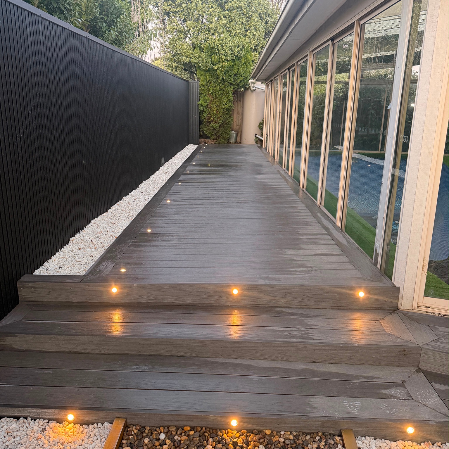 Grey decking with integrated step lighting beside a glass wall