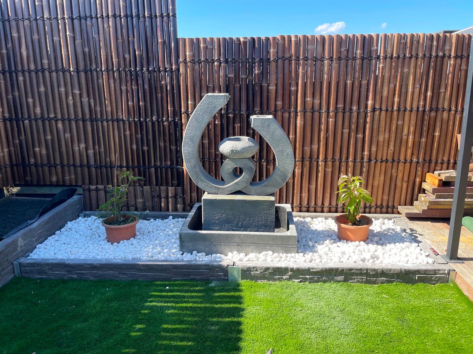 Sculptural garden water feature framed by white pebbles and screening