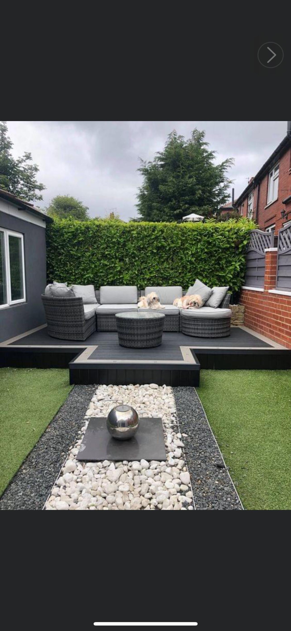 Raised grey deck with curved outdoor seating, two dogs and a pebble garden feature