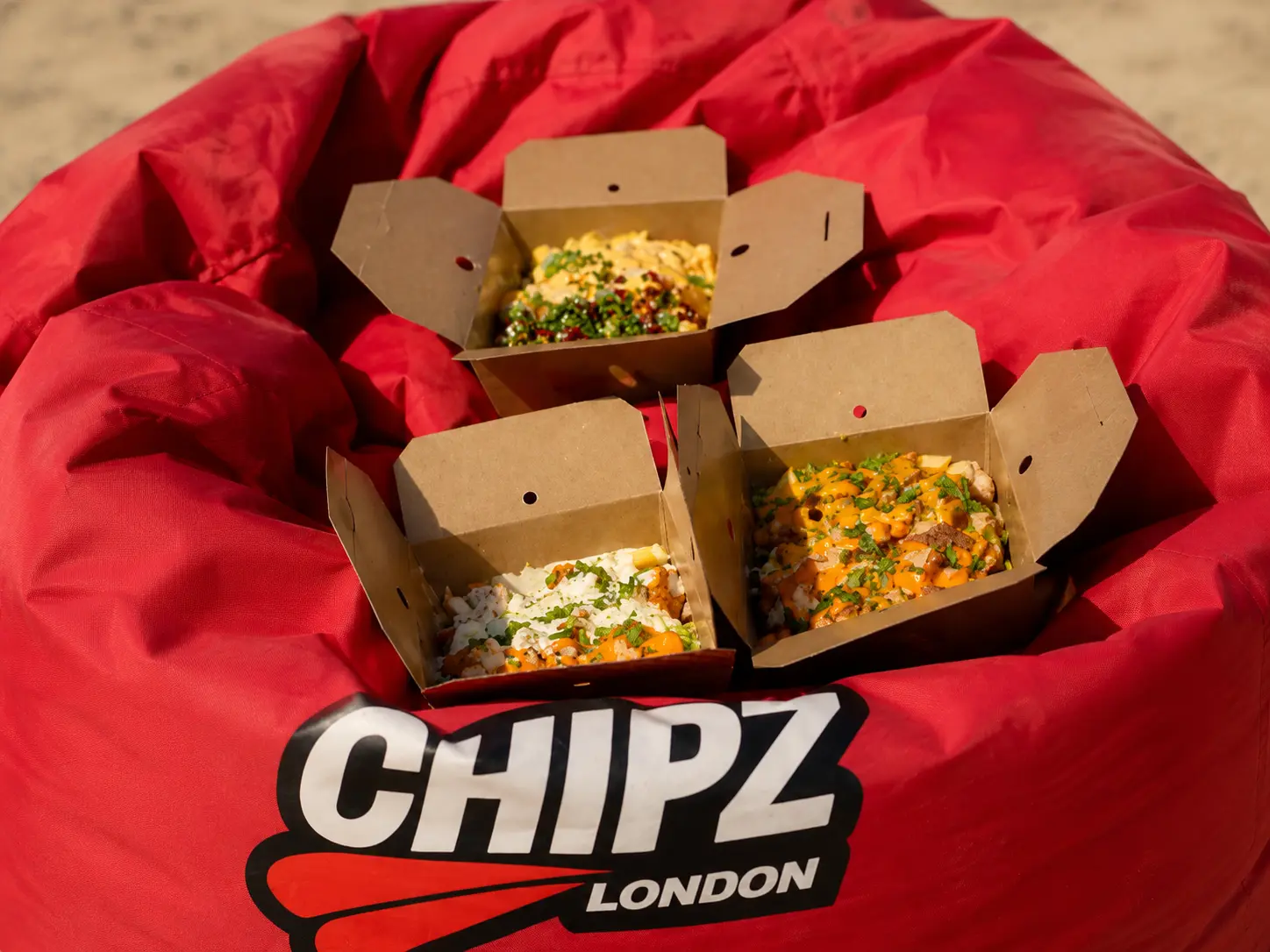 Three boxes of loaded CHIPZ with sauces and toppings on a red CHIPZ London branded seat