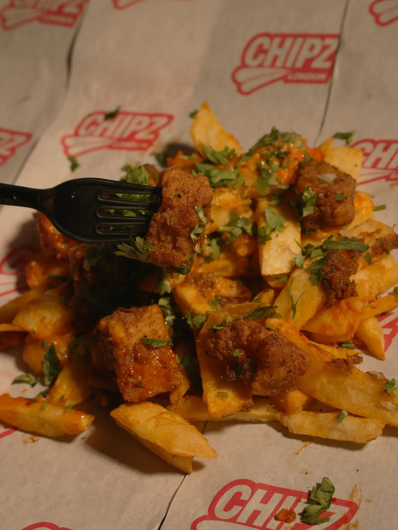 Crispy chicken pieces and thick-cut CHIPZ with sauce and fresh herbs on CHIPZ London branded paper