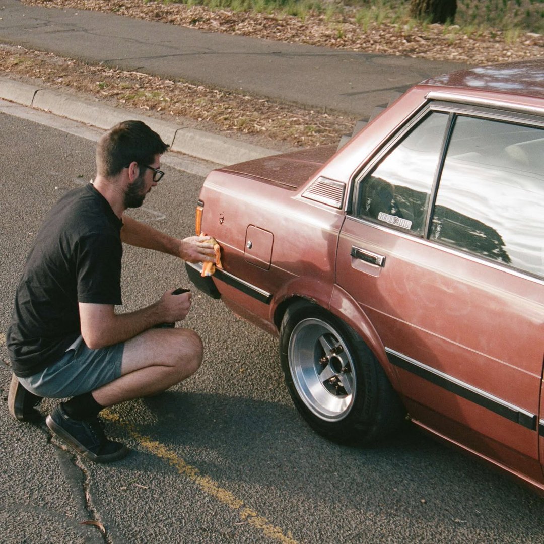 kneeling next to rear of ke70 corolla car