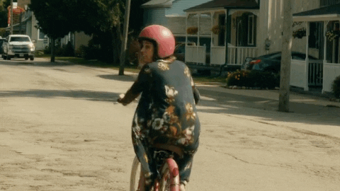 GIF: Alexis is very wobbly as she rides the bike for the first time without Mutt's support. (Schitts Creek)