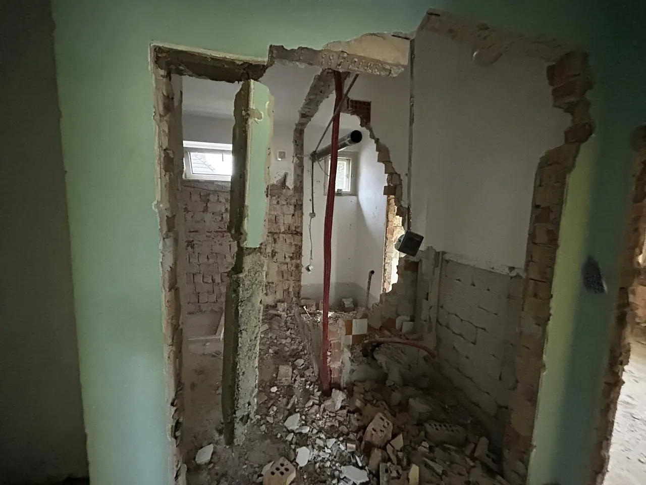 A Veszprémben található Farkas-Konstrukt Kft. generálkivitelezési projekthez készült kép egy bontási munkálatot mutat be. A felvételen látható, hogy a falak részben lebontásra kerültek, a padlón törmelék és építőanyagok hevernek. A helyiségben látható a bontási folyamat nyomai, a falakon csövek és vázszerkezetek láthatók, ami a generálkivitelezés folyamatát tükrözi.