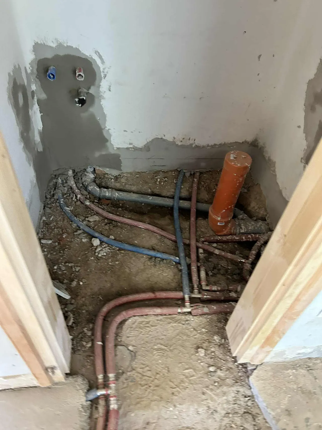 A képen egy építkezési terület látható Győrben, ahol a Farkas-Konstrukt Kft. generálkivitelezési munkálatait végzik. A falban víz- és csatornázási vezetékek találhatók, valamint egy narancssárga PVC cső, amely az injektálás folyamatához kapcsolódik. A környezetben látható a friss vakolat, és a padlónál építési törmelék is látható.